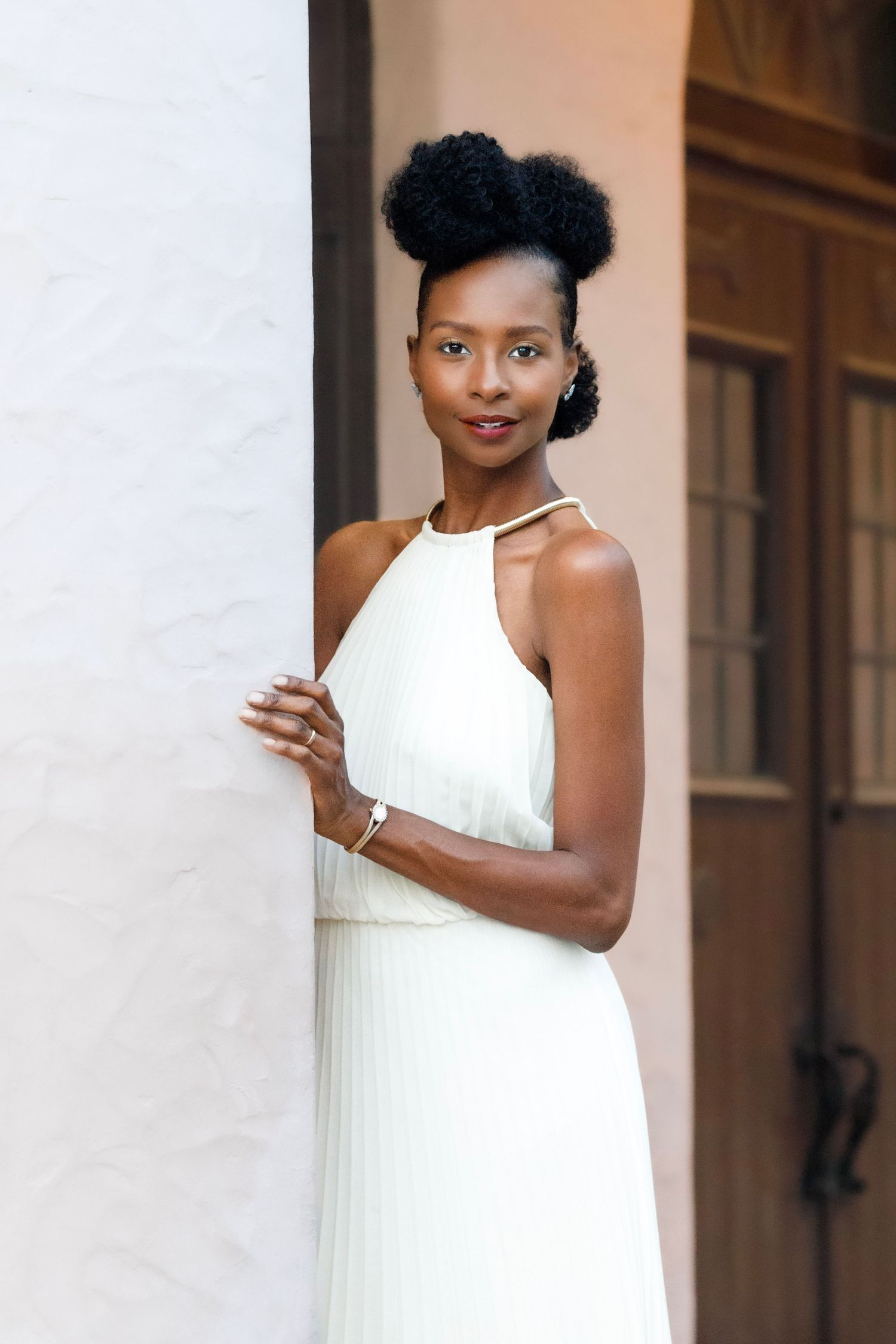 Woman in elegant white sleeveless dress poses confidently against a neutral background.