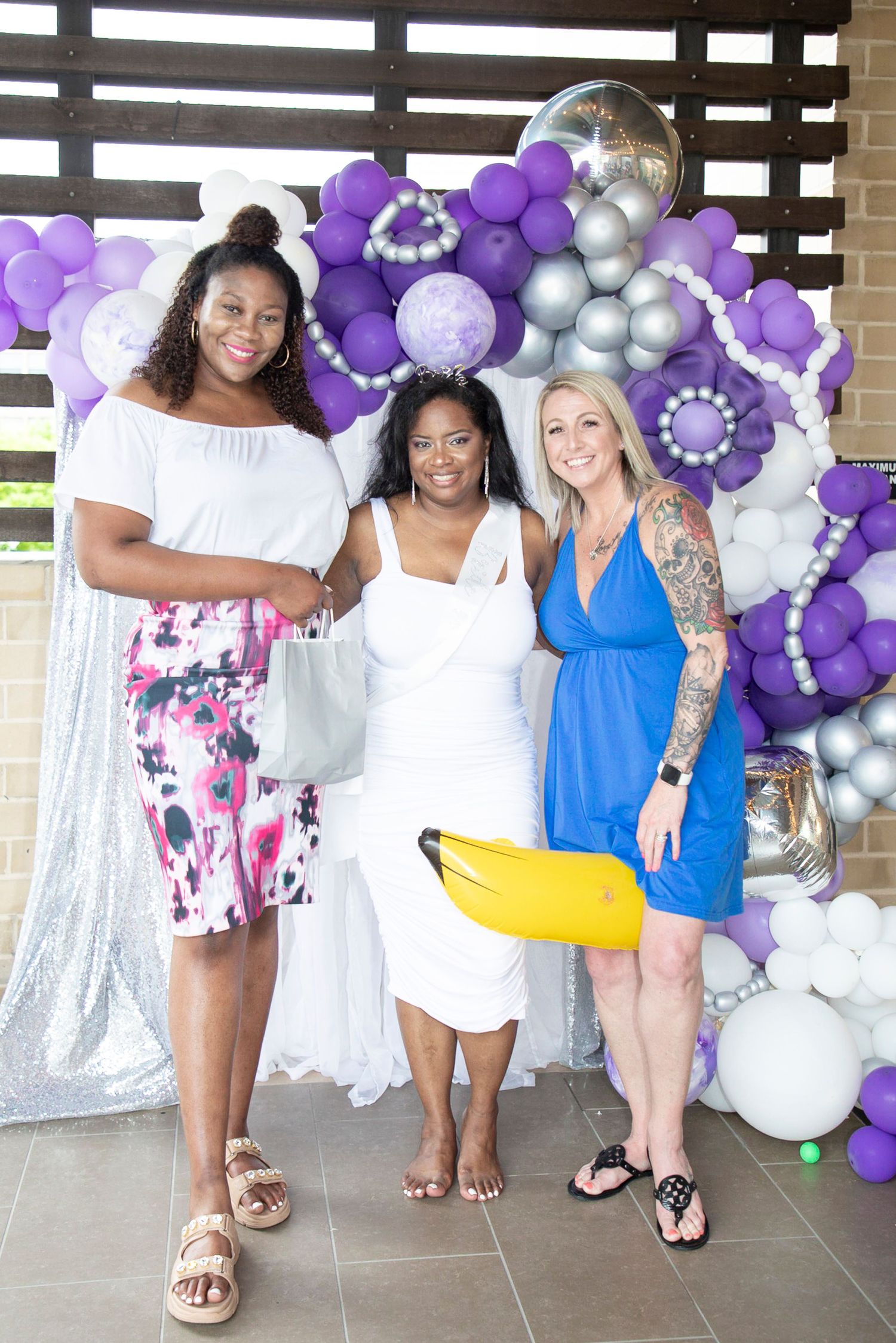 A group poses in front of a purple and silver balloon arch display at a celebration event.