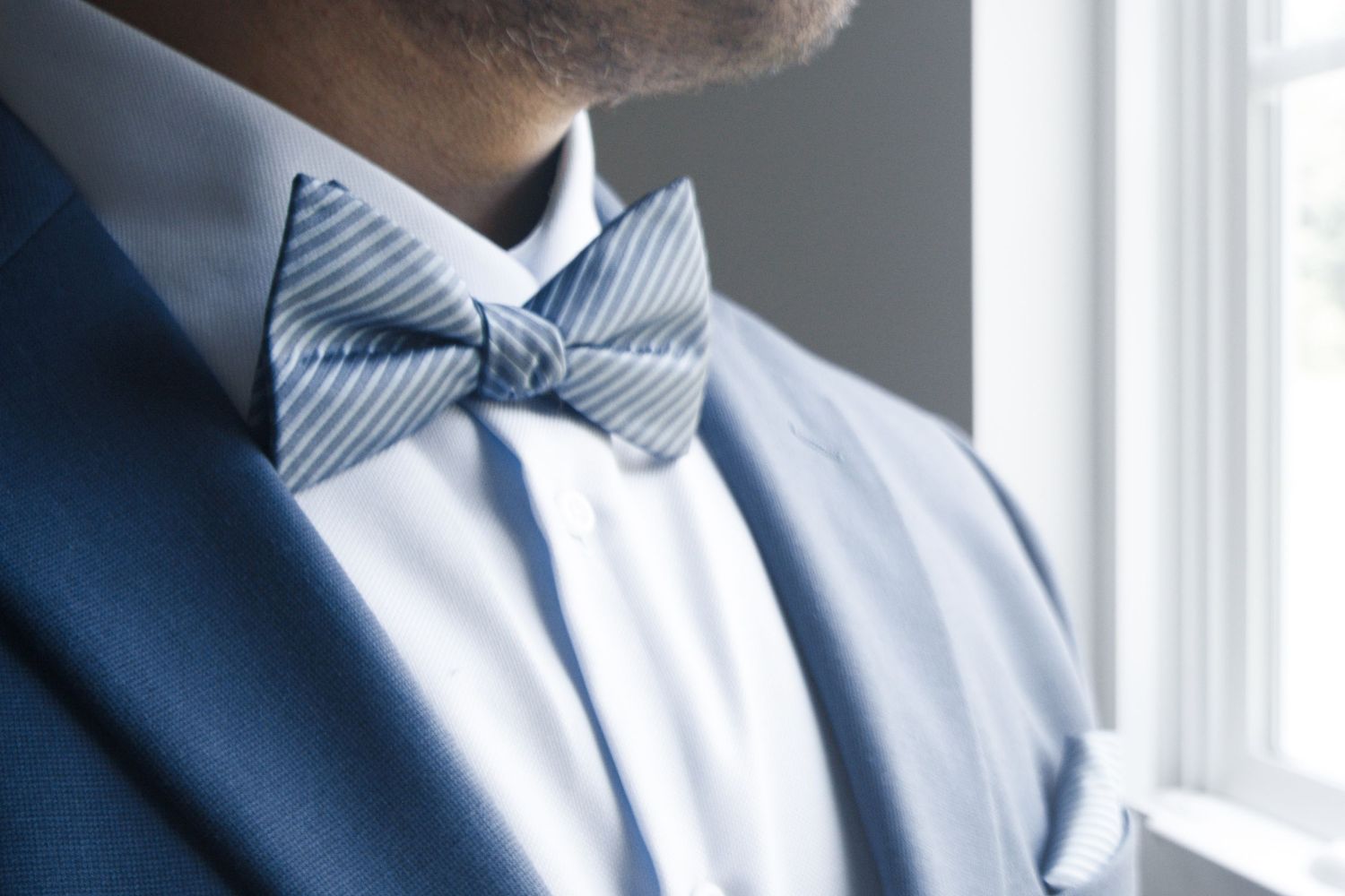 Man wearing a blue striped bow tie with a white dress shirt and navy blue suit jacket.