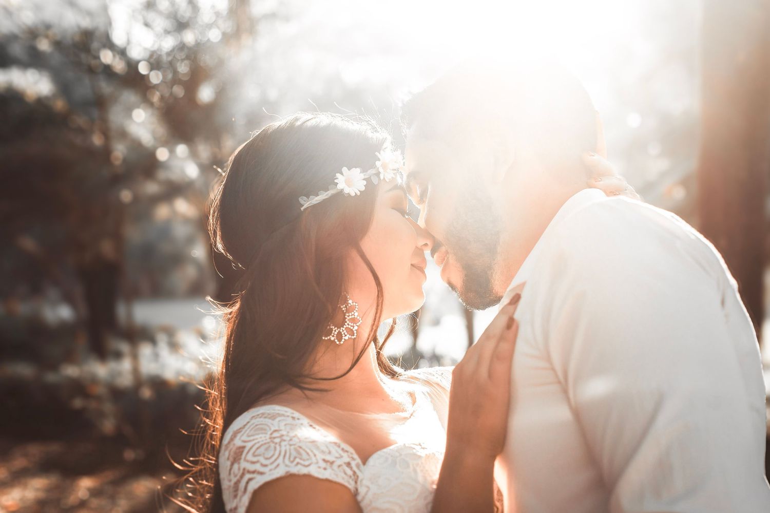 A romantic couple in wedding attire share an intimate moment in golden sunlight filtering through trees.