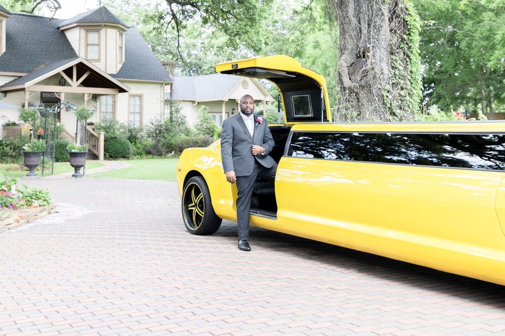 Man in gray suit standing beside a striking yellow stretch limousine on a brick driveway near a elegant house.