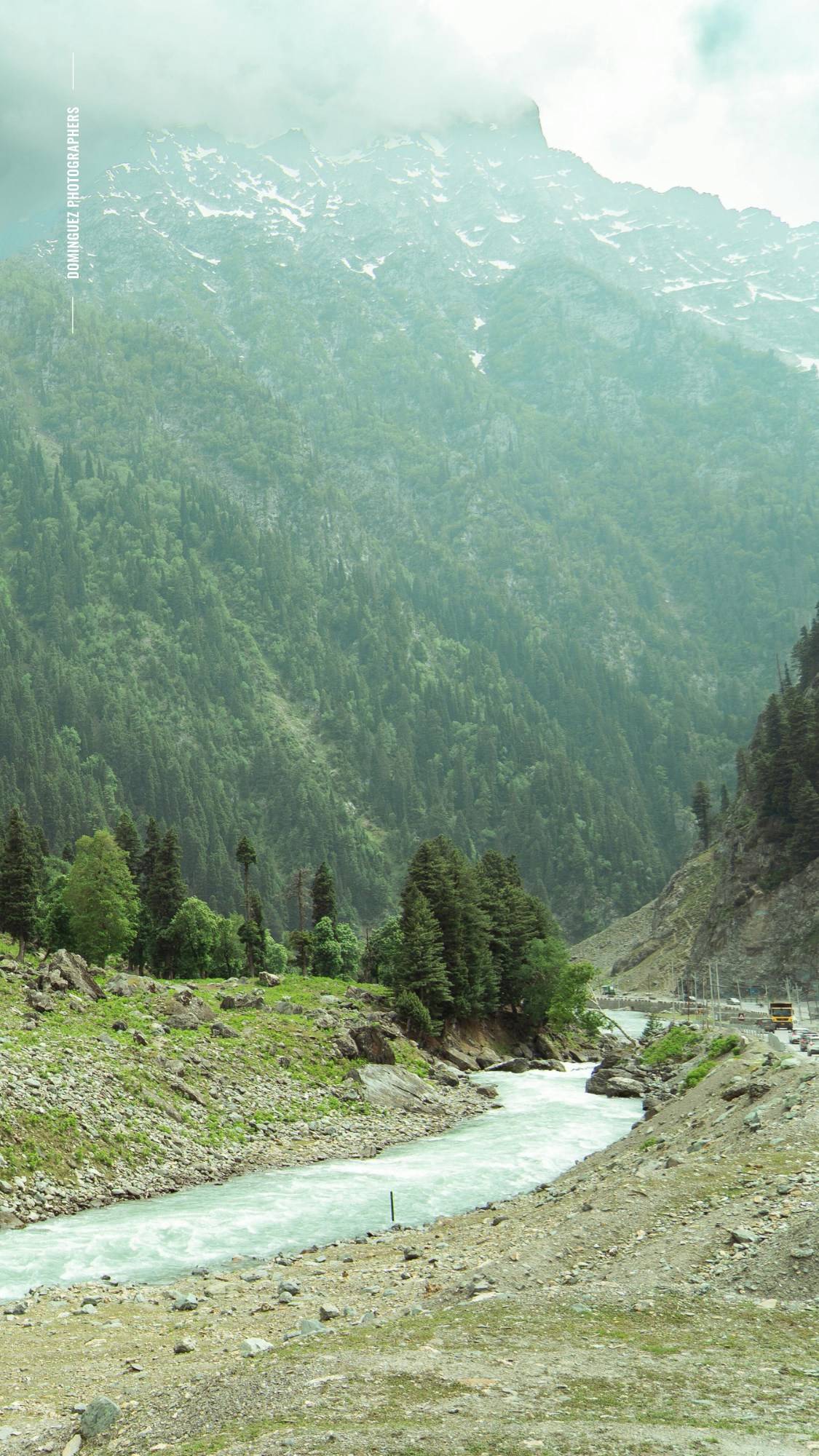 A winding turquoise river flows through a mountainous valley with evergreen trees and rocky terrain in Kashmir.