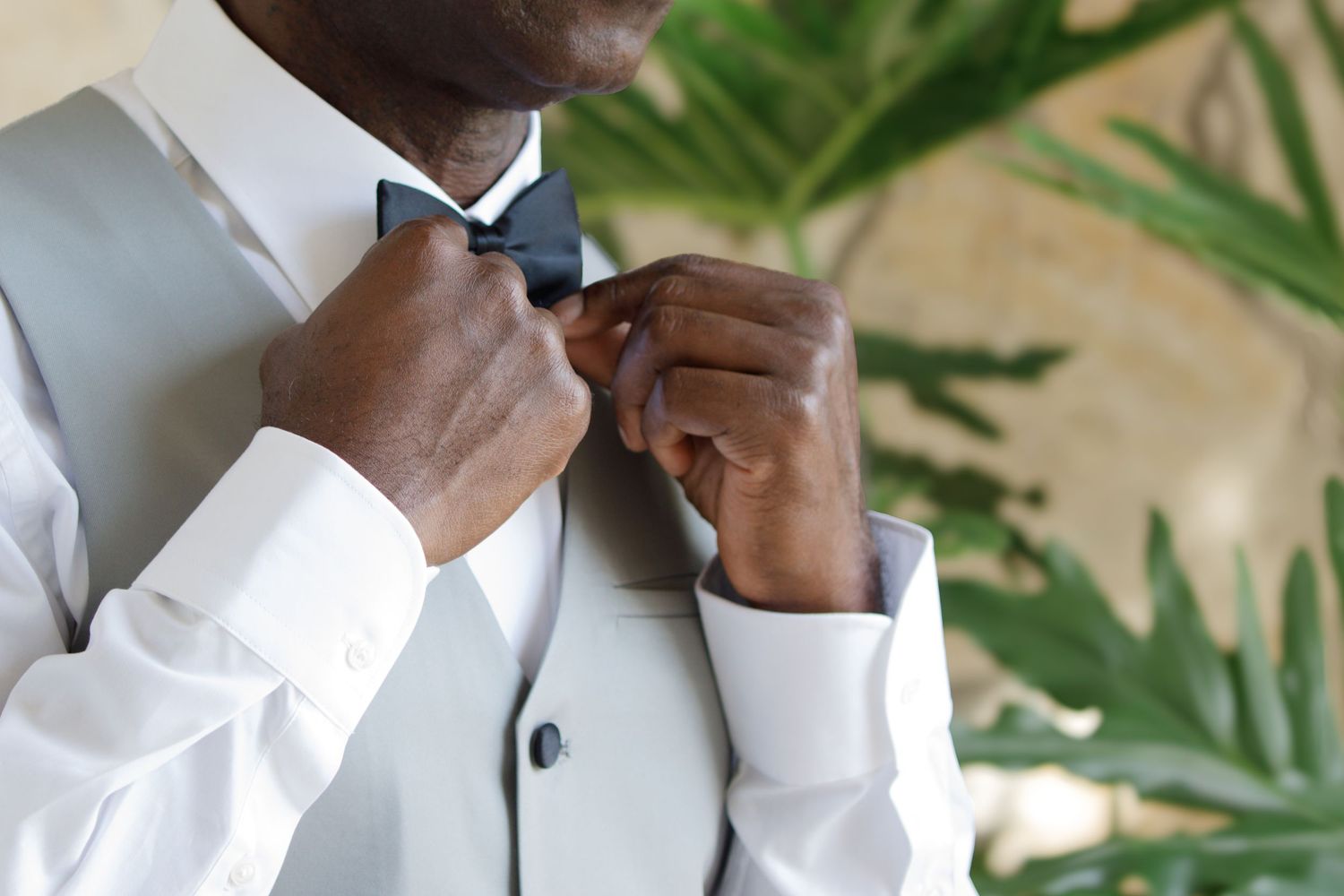 Man in gray suit adjusting black bow tie, getting dressed for formal event or wedding.