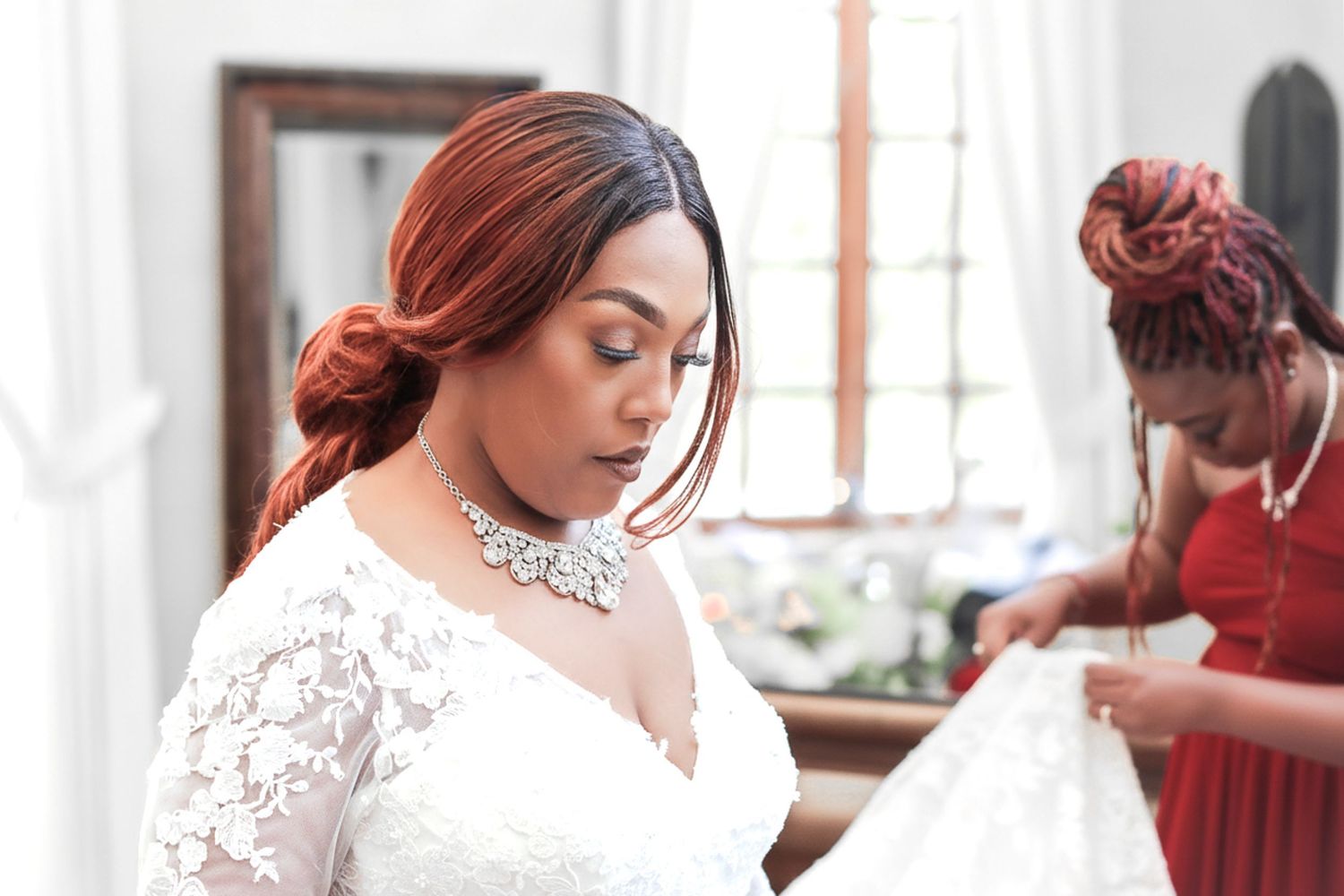 A woman in a white lace wedding dress poses in a bright interior setting with natural light.