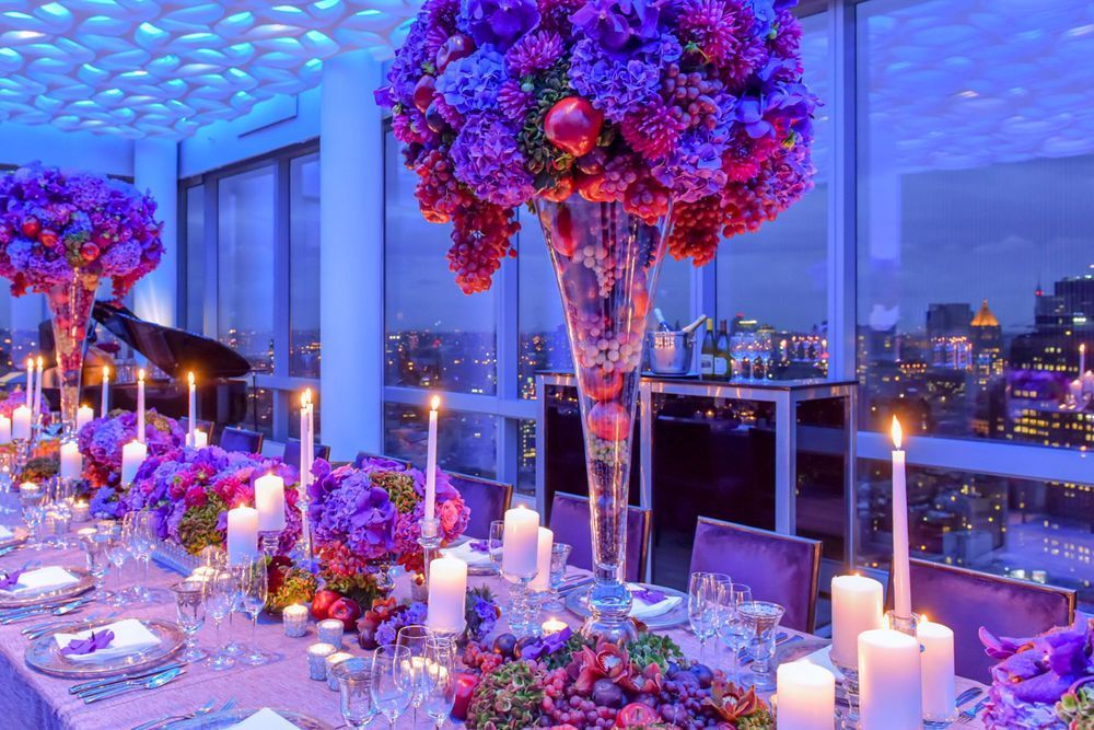 Luxurious wedding reception venue with purple and blue lighting, crystal chandeliers, and red floral centerpieces.