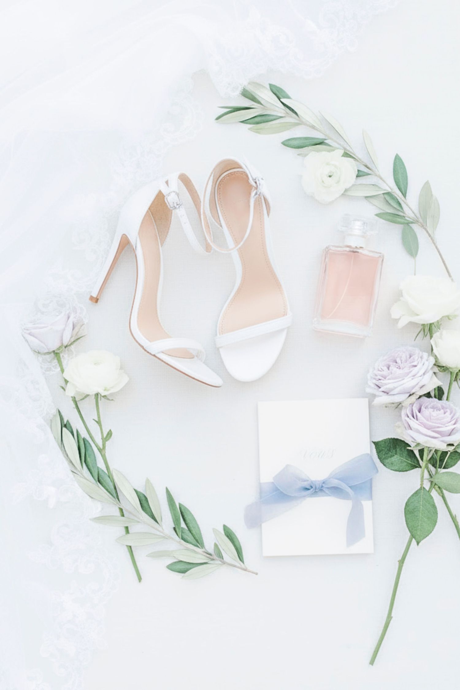 White wedding shoes arranged with delicate roses and eucalyptus leaves on a light background.