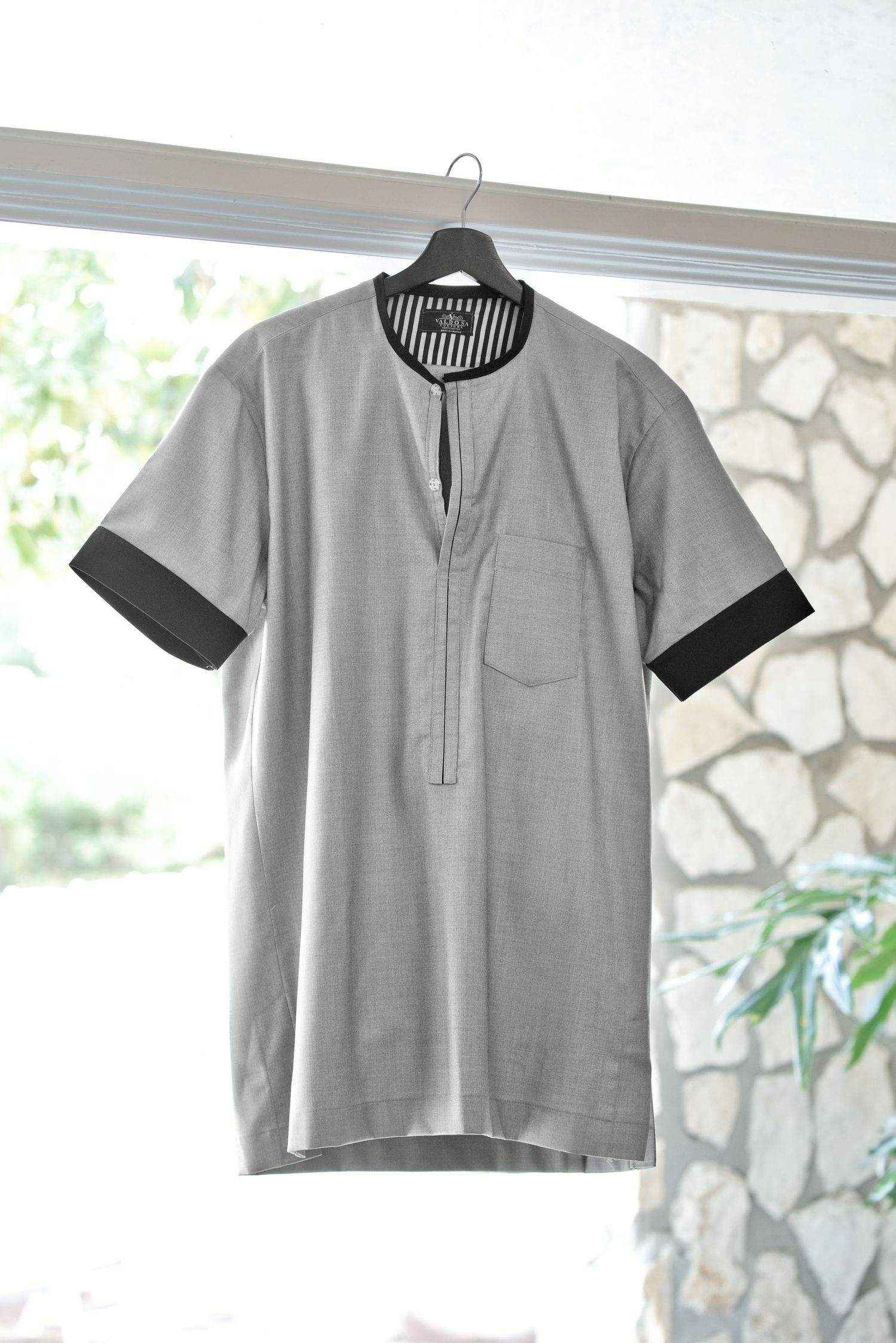 Gray short-sleeve pullover shirt with black trim cuffs, striped collar, and chest pocket hanging on a hanger.