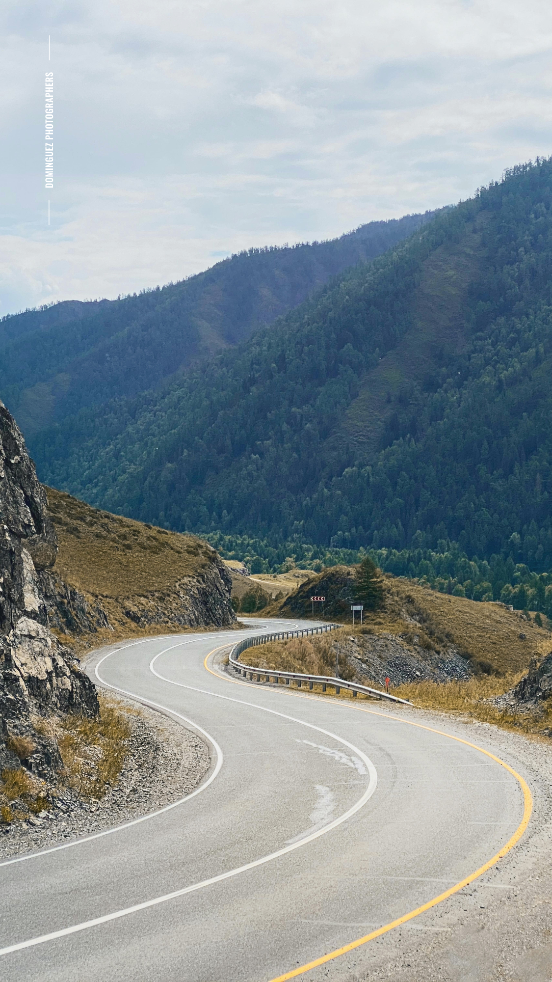 Winding mountain road curves through scenic mountainous terrain with steep cliffs and yellow dividing lines.