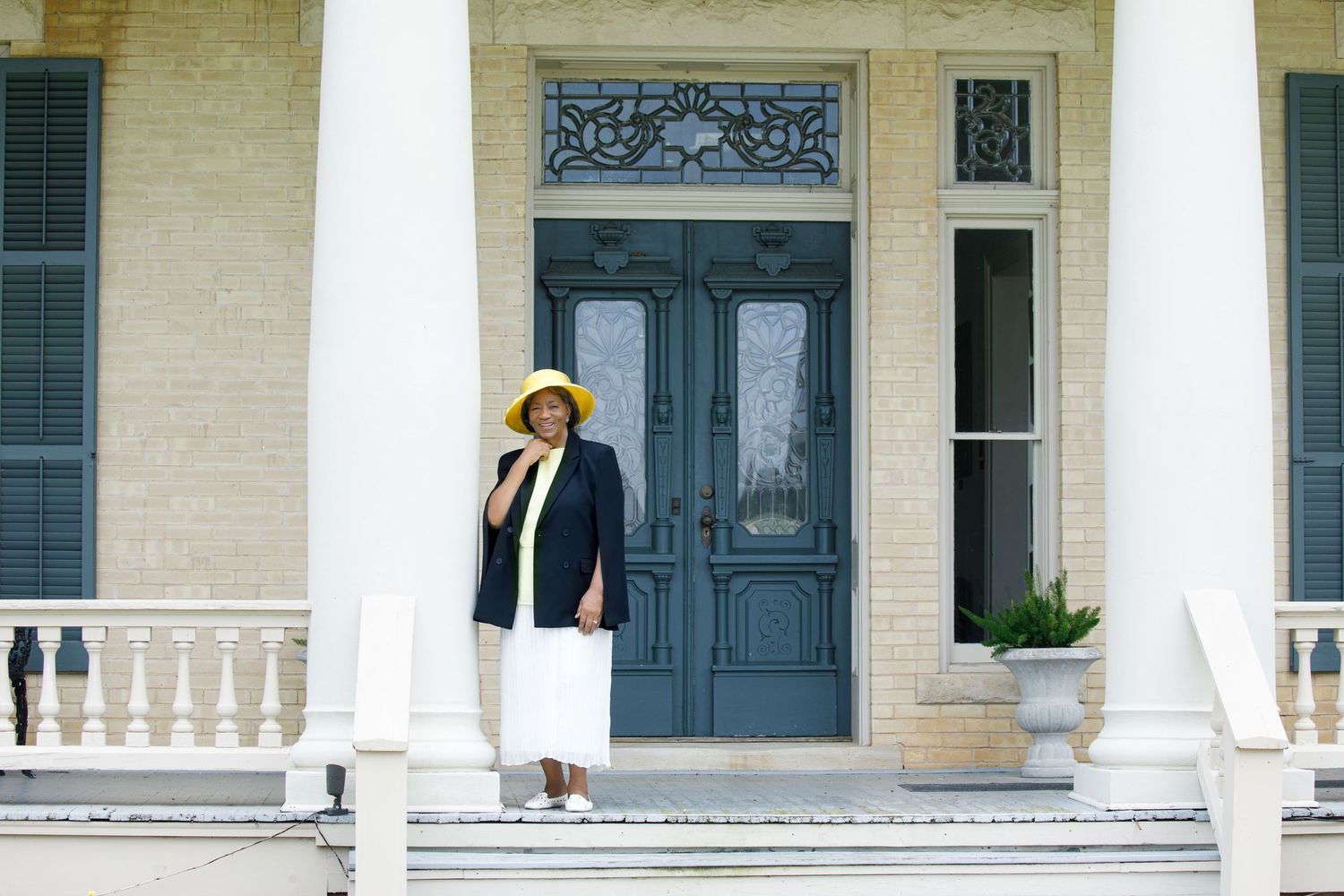 Historic white mansion with elegant columns and blue doors features a wraparound porch and ornate architectural details.