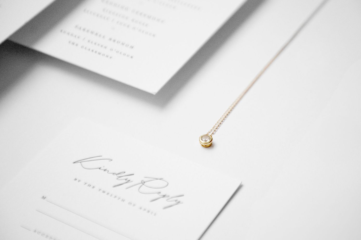Elegant minimalist white wedding stationery with delicate gold necklace photographed from above.