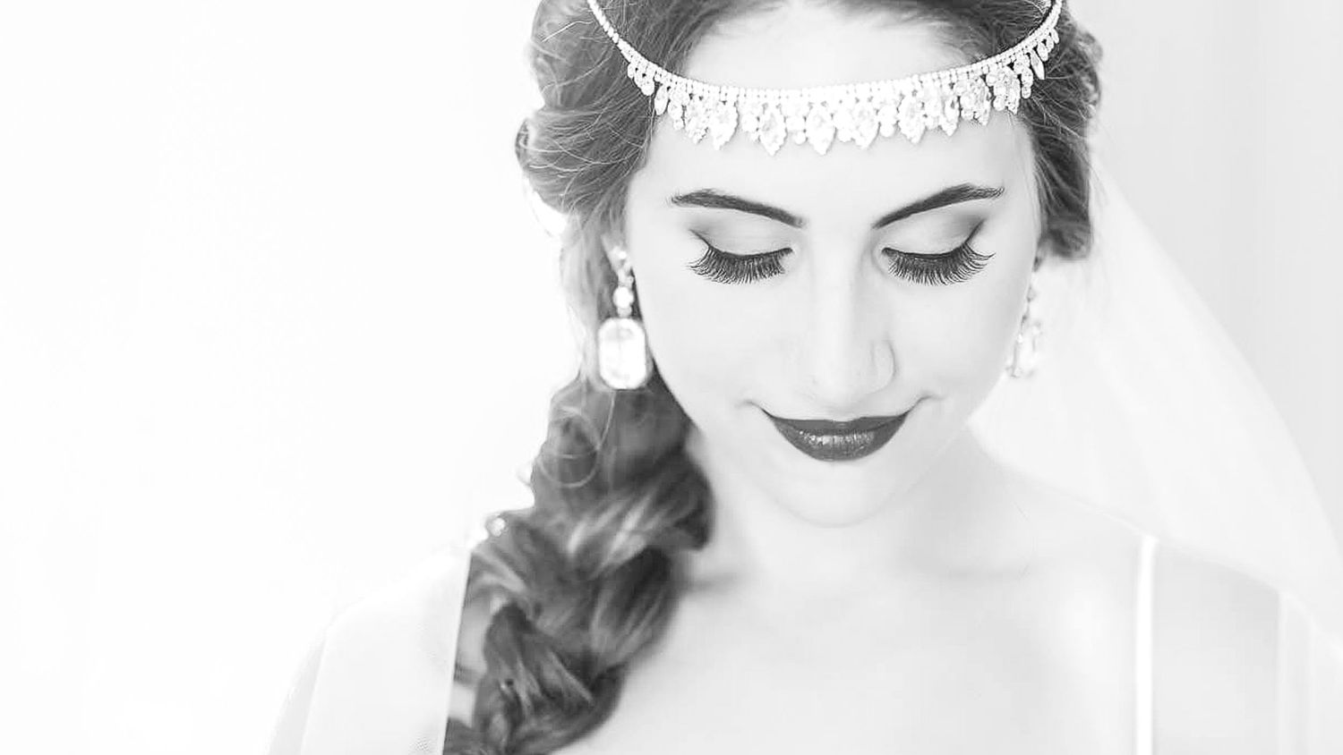 Black and white portrait of a bride wearing a crystal tiara and veil, with elegant makeup and braided hair.