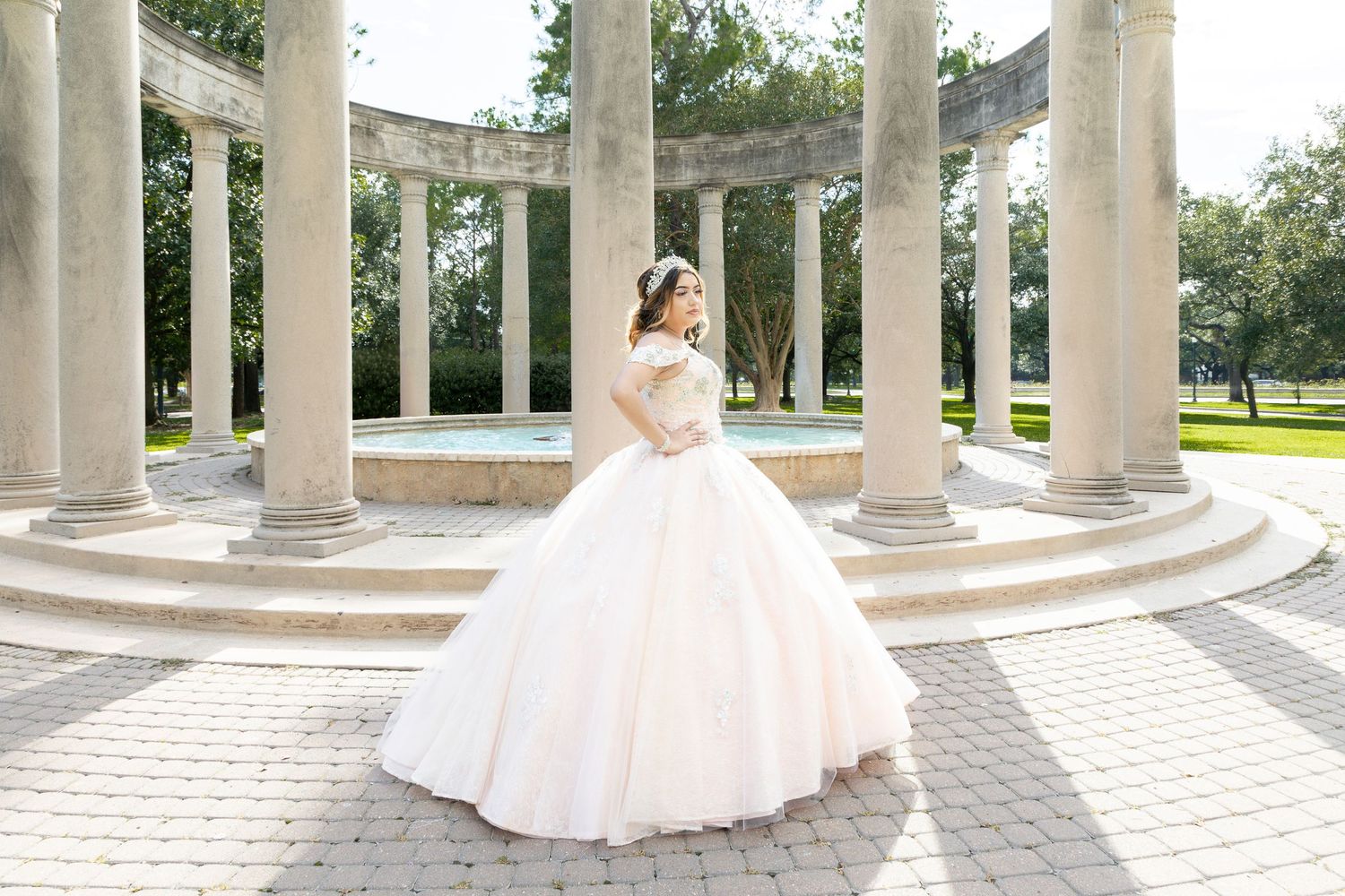 Young woman in a white ballgown poses gracefully among elegant stone columns in an outdoor garden setting.