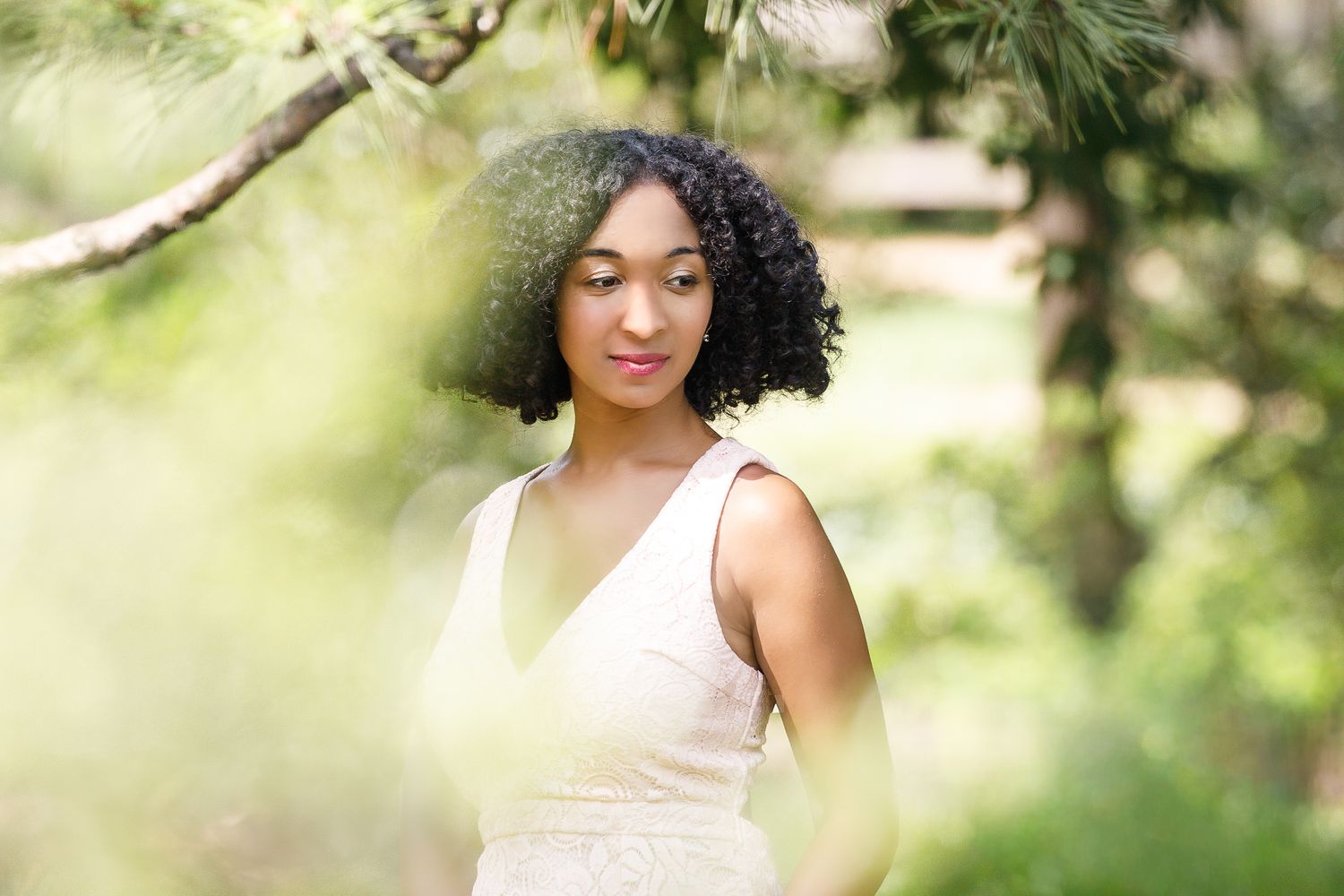 A person in a white dress poses outdoors among lush greenery and natural lighting for a portrait session.