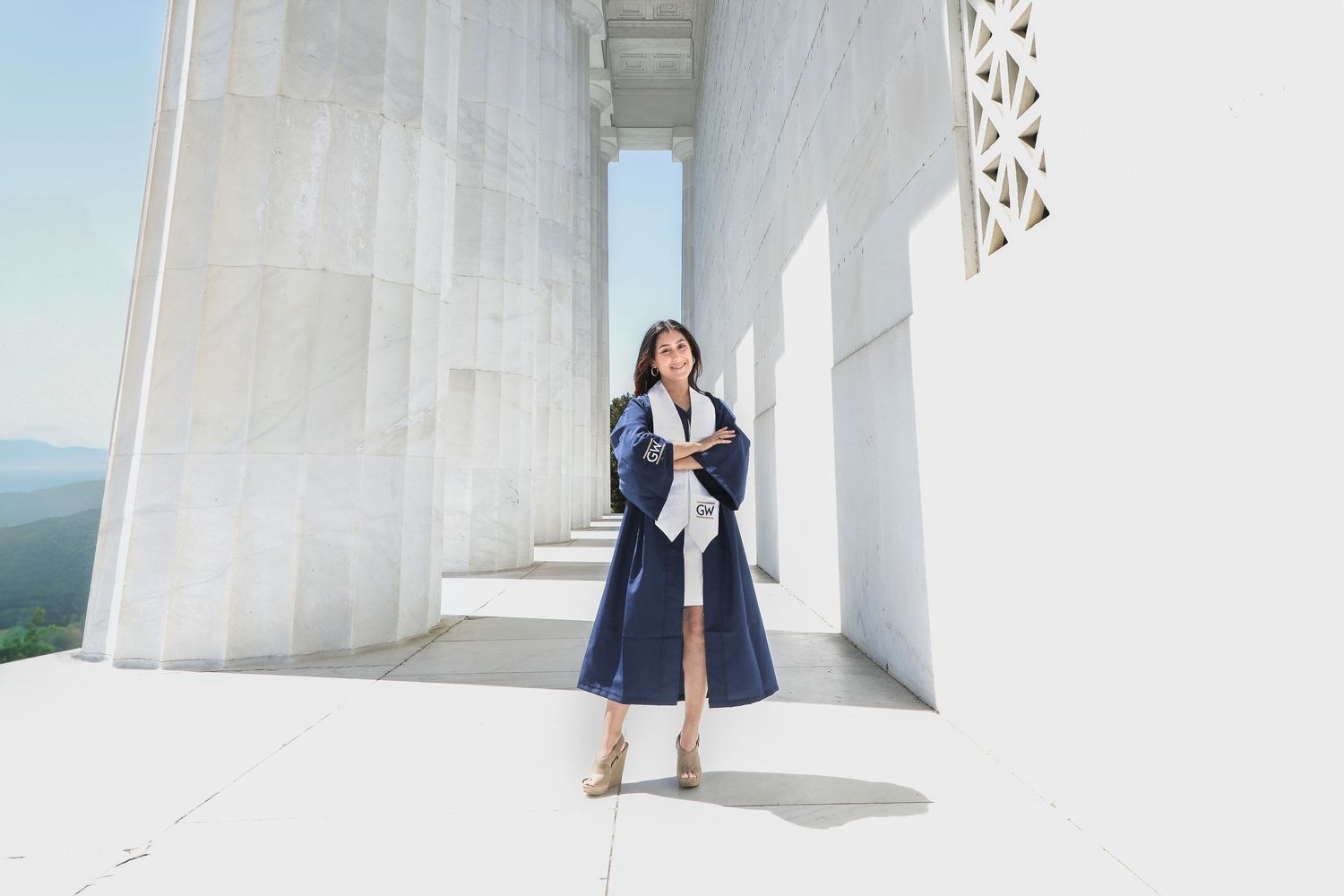 Person in navy blue dress poses against white architectural columns in a bright outdoor setting.