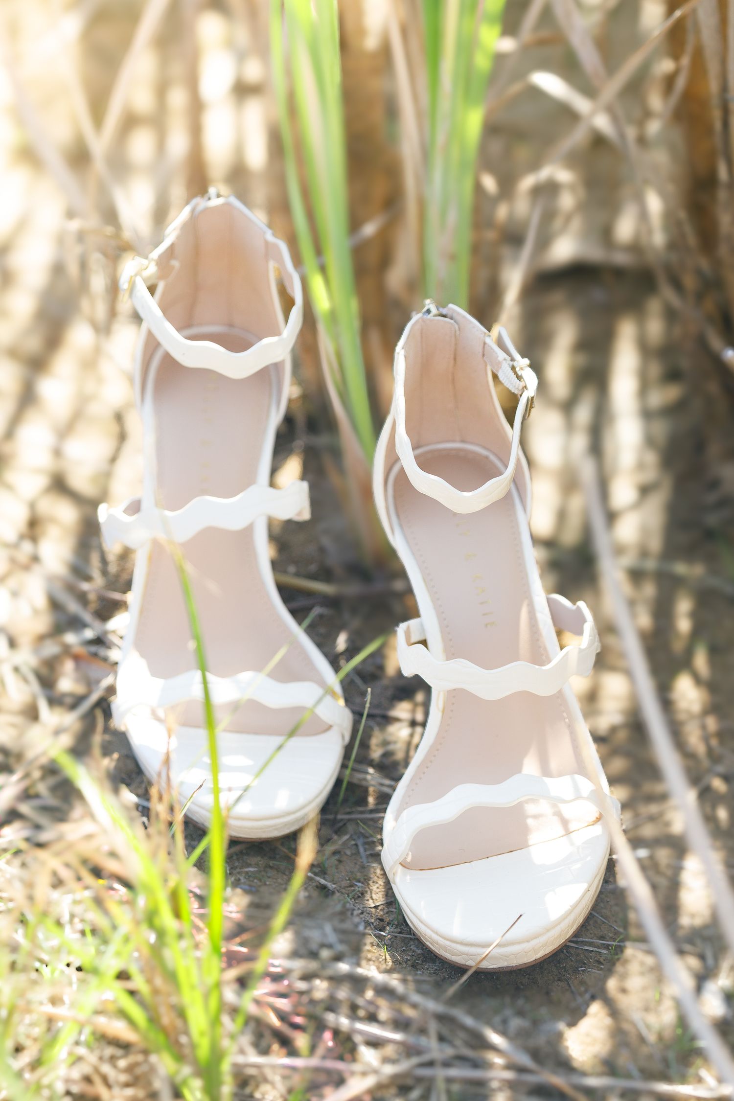 White baby sandals lined up in grass and sunlight creating shadow patterns on the ground.