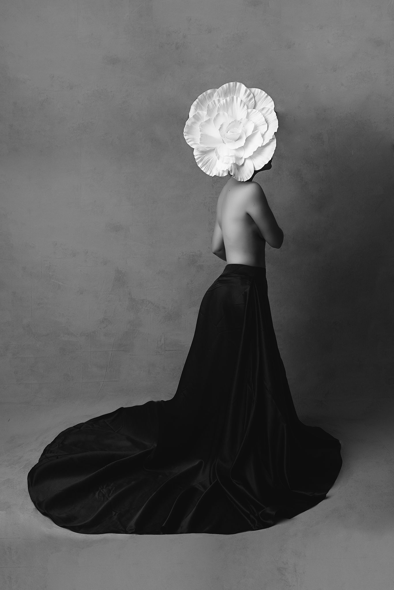 Surreal black and white art photograph of a topless figure wearing long black skirt with white flower as head.