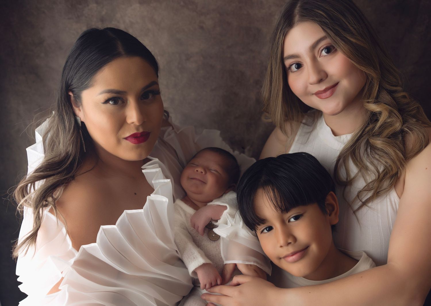 Portrait of family in white clothing with baby and young boy gathered together for studio photograph.