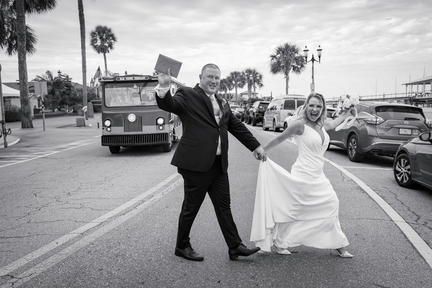 A black and white sequence of wedding photos showing a couple  joyfully crossing the street with a St Augustine trolley.