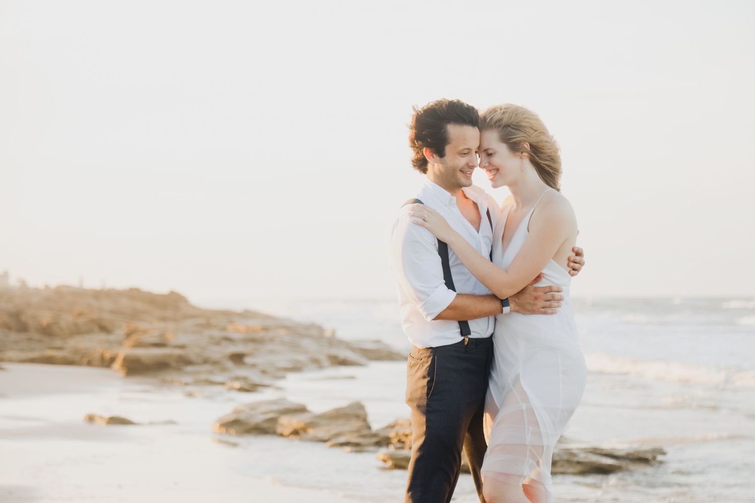 A couple who elopes in St Augustine embraces on a rocky beach at sunset in romantic along St Augustine Beach.