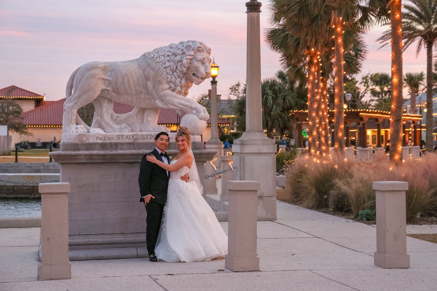 A newly married couple elopes posing at sunset in front of the Bride of Lions statues in St Augustine.
