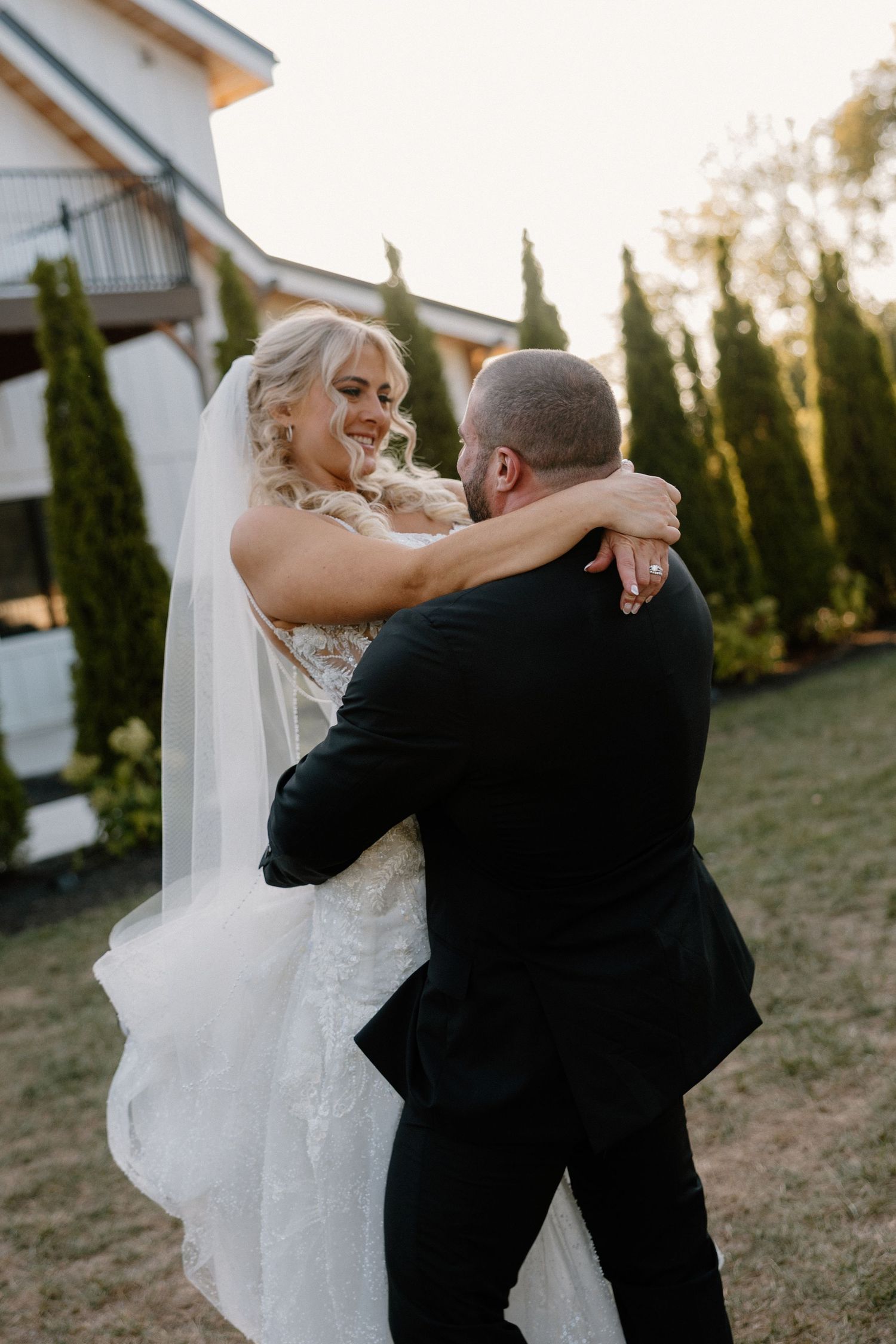 A bride and groom share a tender dance moment outdoors at their wedding celebration as the sunlight filters through trees.