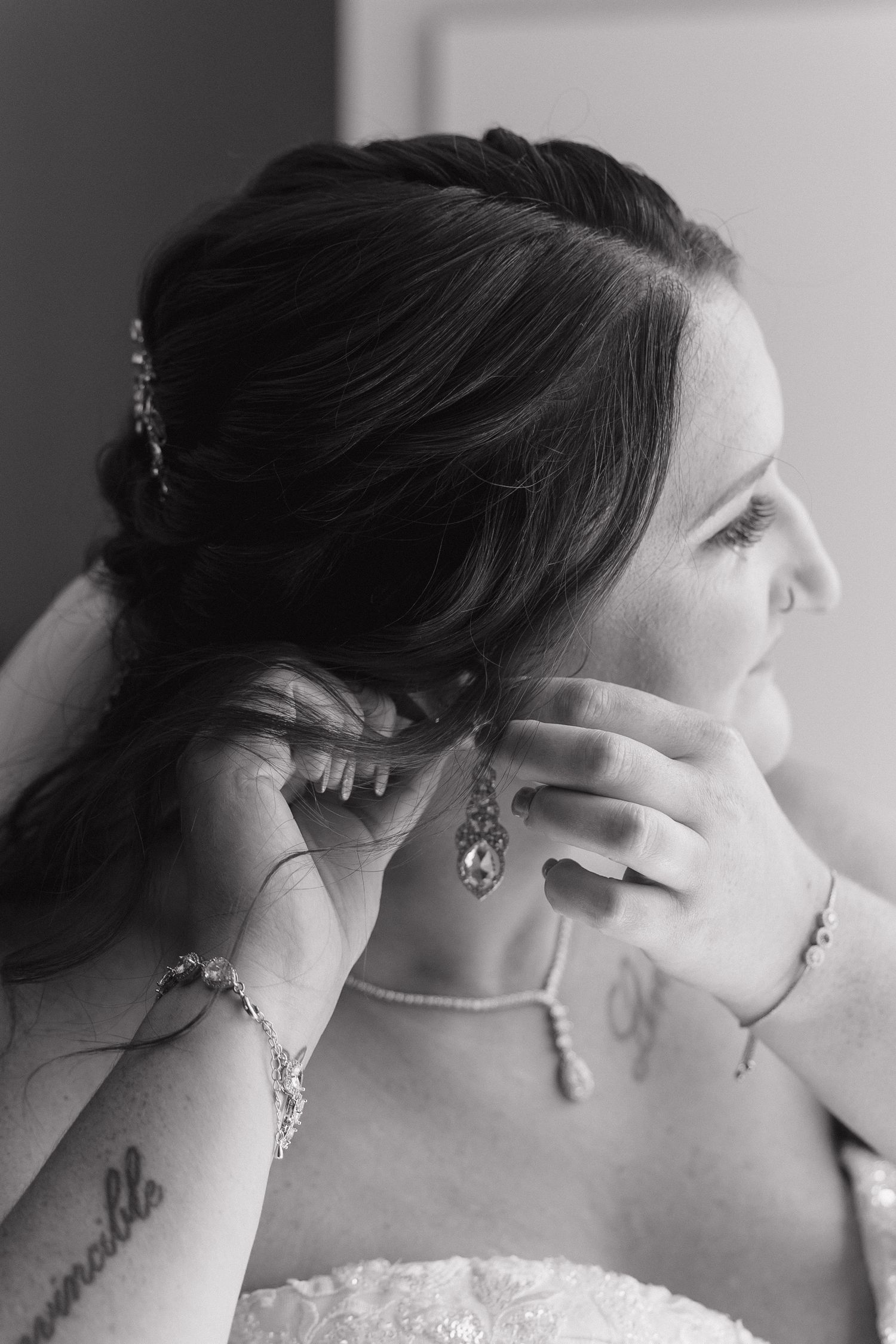 Black and white photo of someone putting on jewelry while wearing a strapless dress.