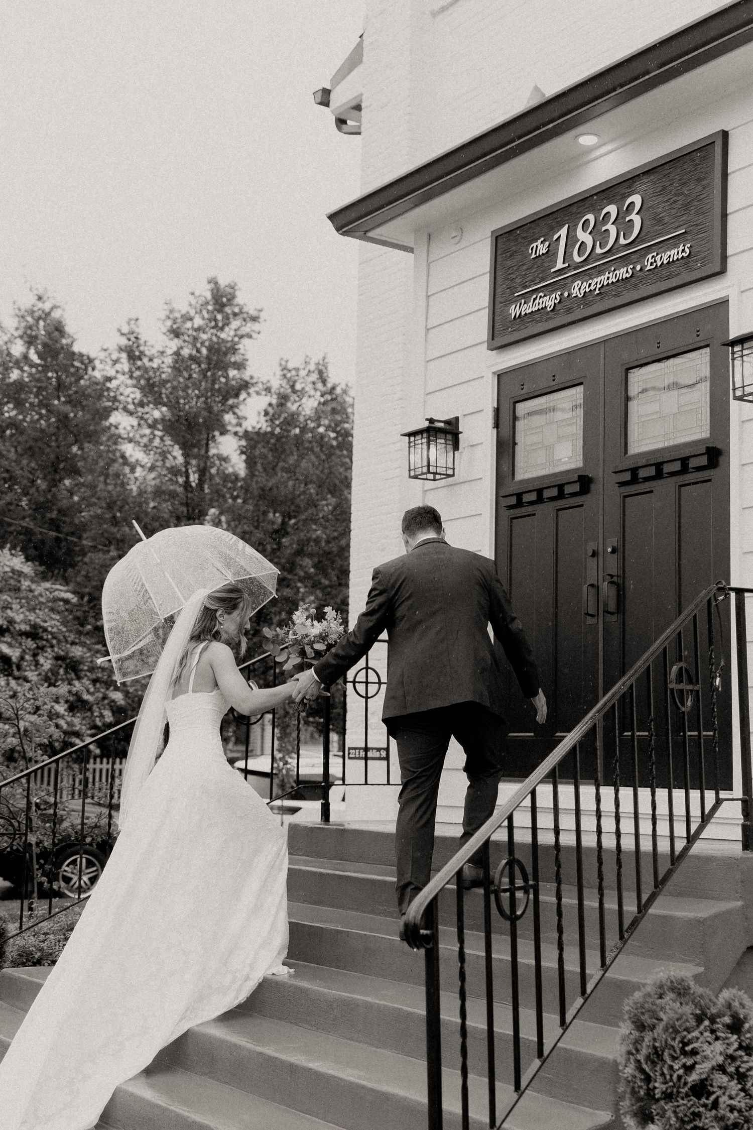 A couple in wedding attire ascends the steps of a historic white building marked with '1835' above the entrance.
