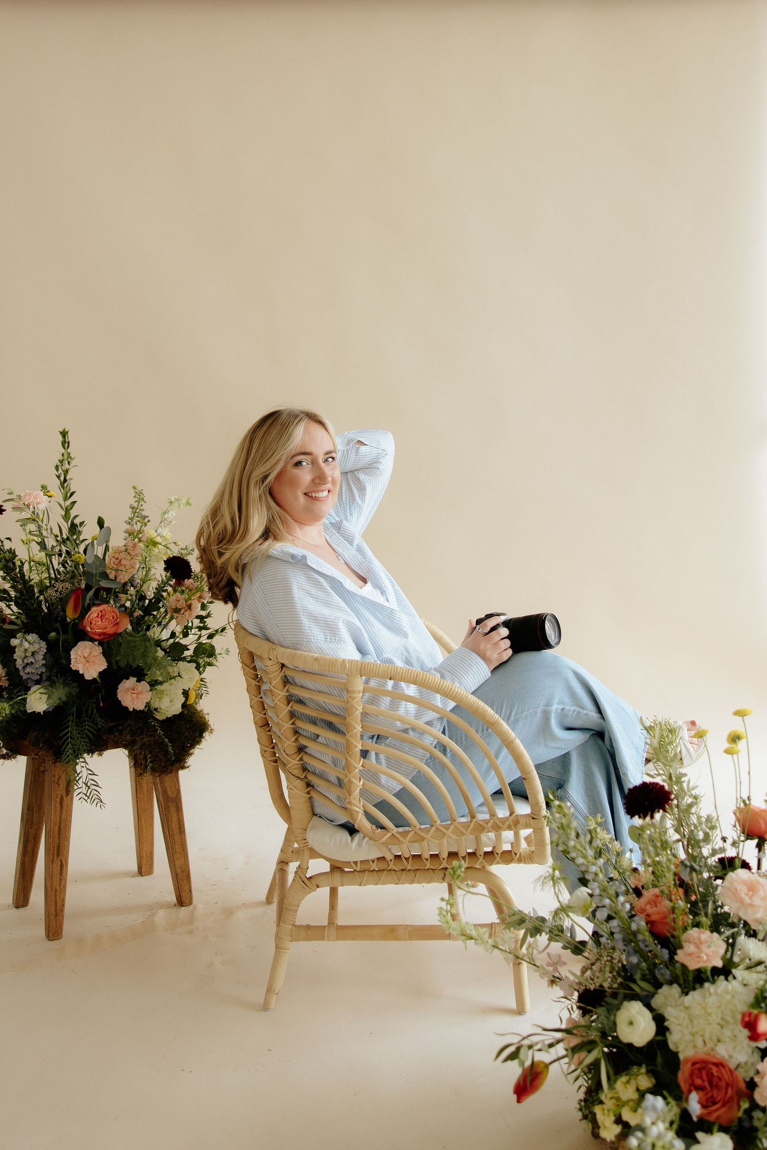 A person relaxes in a rattan chair surrounded by elegant floral arrangements in a bright studio setting.
