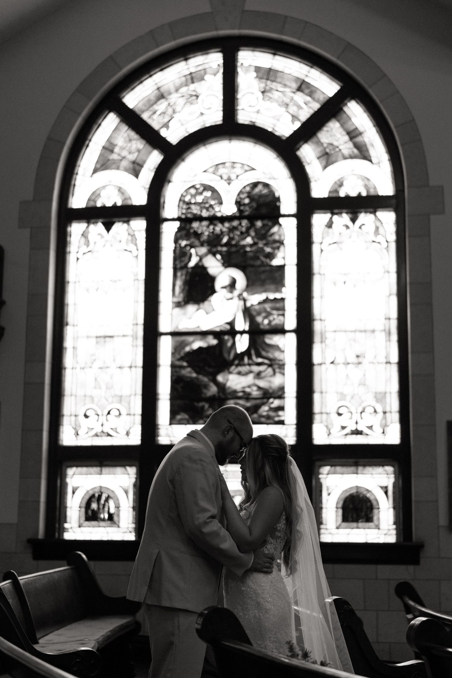A romantic black and white photo series showing a couple embracing by ornate arched church windows.