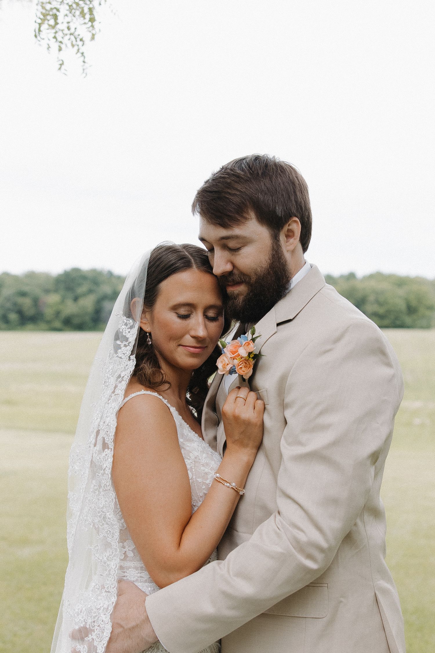 A romantic wedding portrait of a couple in a field with the bride in white lace and groom in beige suit.