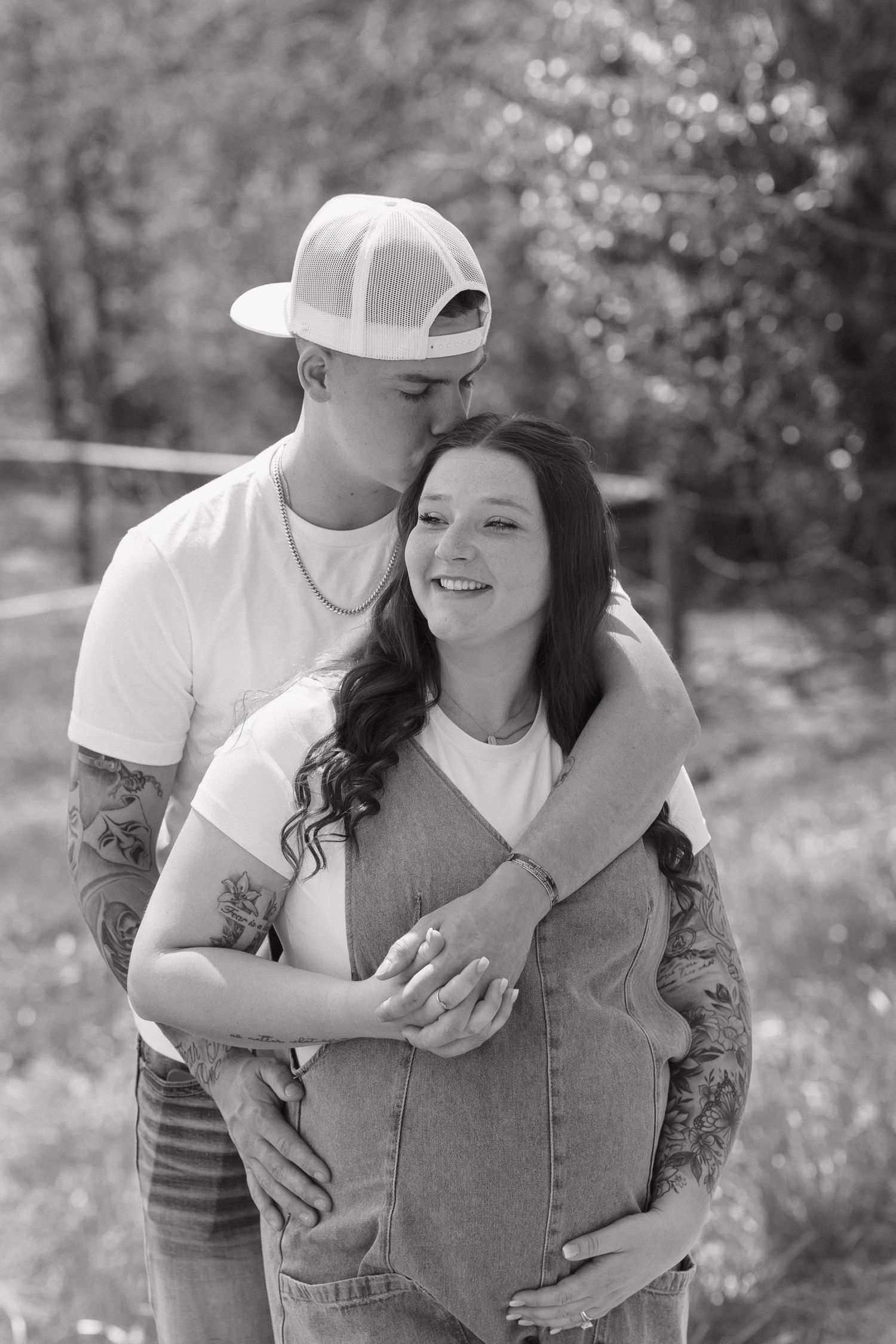 A black and white maternity photo shows a loving couple embracing outdoors amidst spring blossoms and nature.