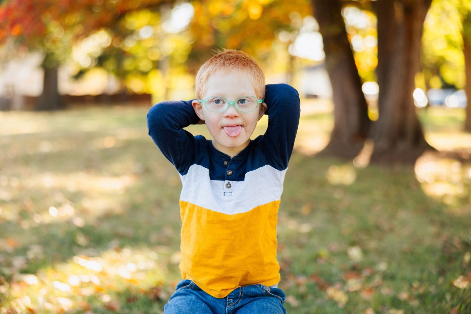 Child in yellow and blue outfit plays outdoors in autumn leaves.