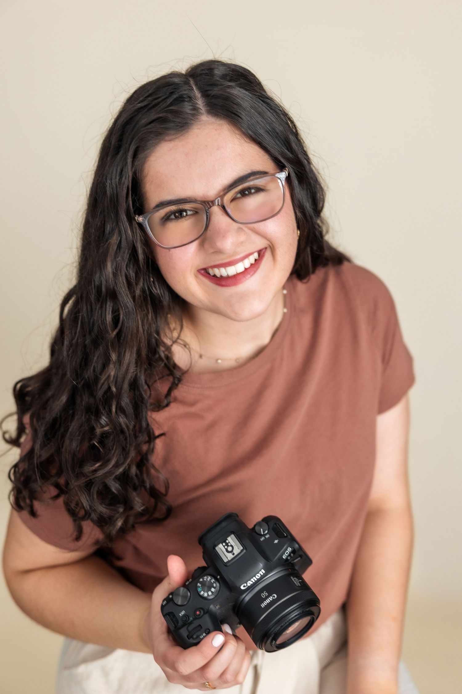 Portrait of a photographer holding a camera while wearing a rust colored shirt.