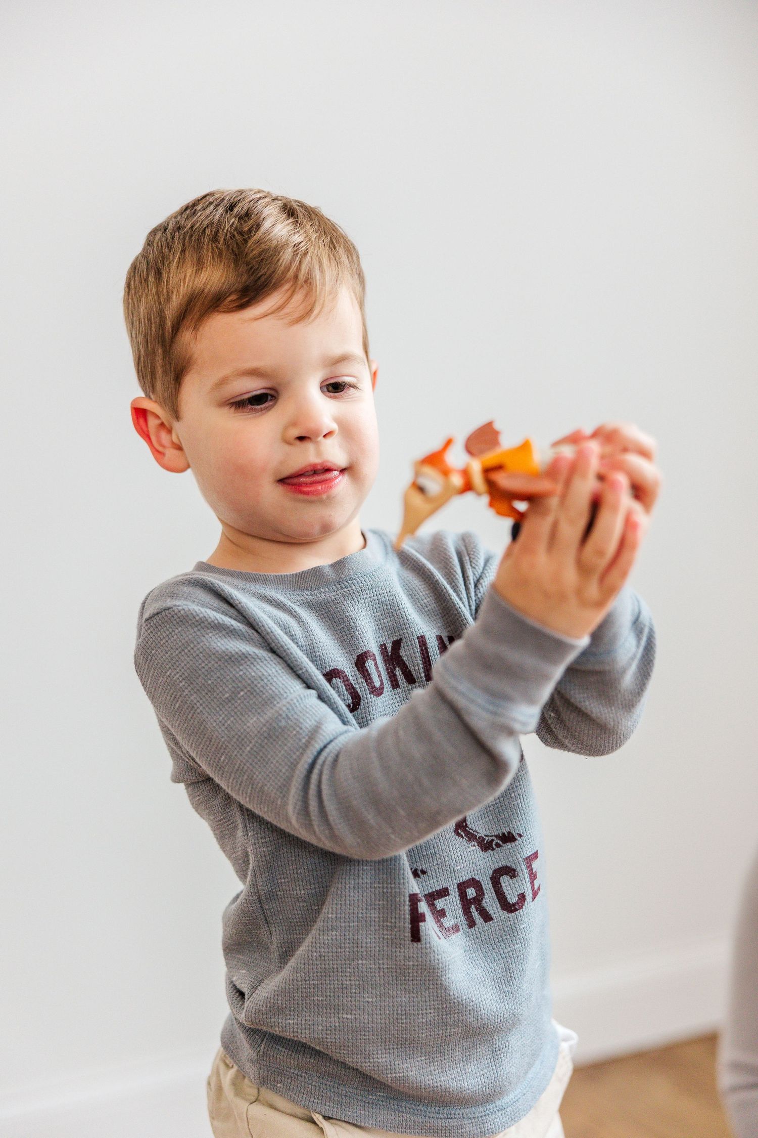 Child in grey sweatshirt plays with orange objects against white background.