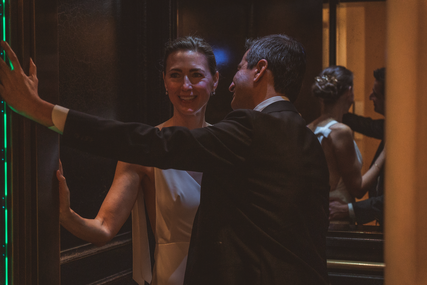 A couple dance together at an event with dramatic lighting and dark formal attire.