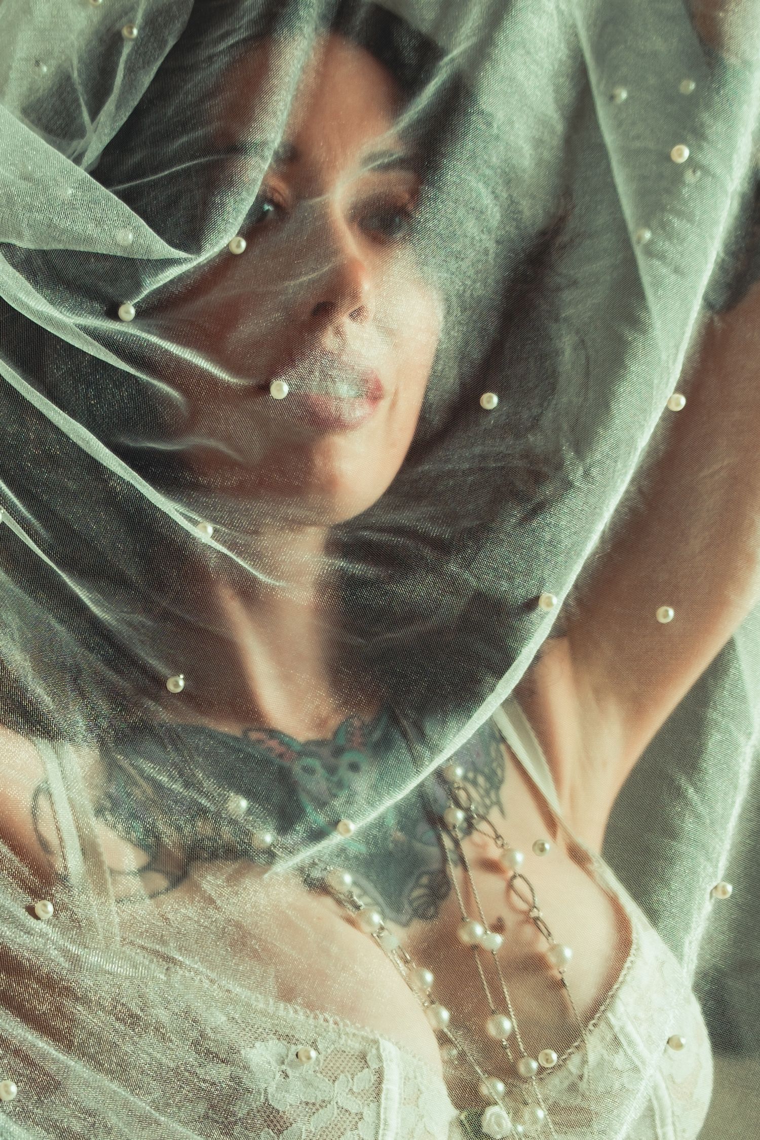 Ethereal close-up portrait through sheer veil with pearl details and soft lighting. bridal boudoir