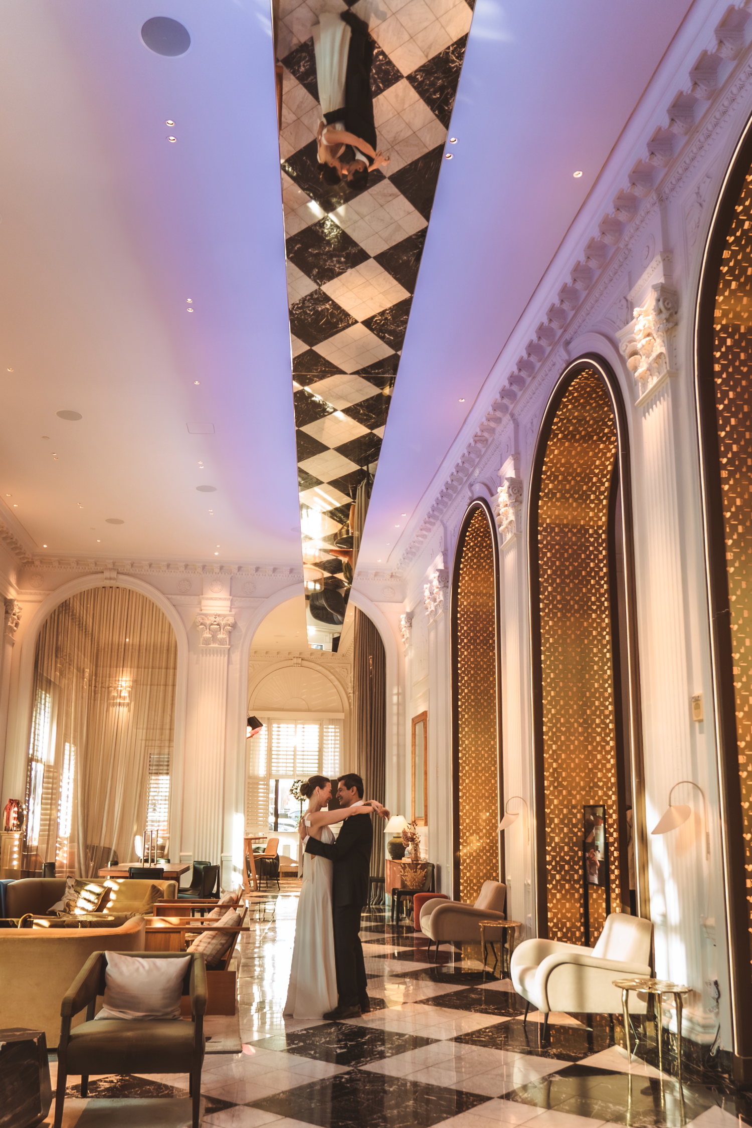 Elegant couple dancing in a luxurious hotel lobby with checkered ceiling and ornate arched doorways.