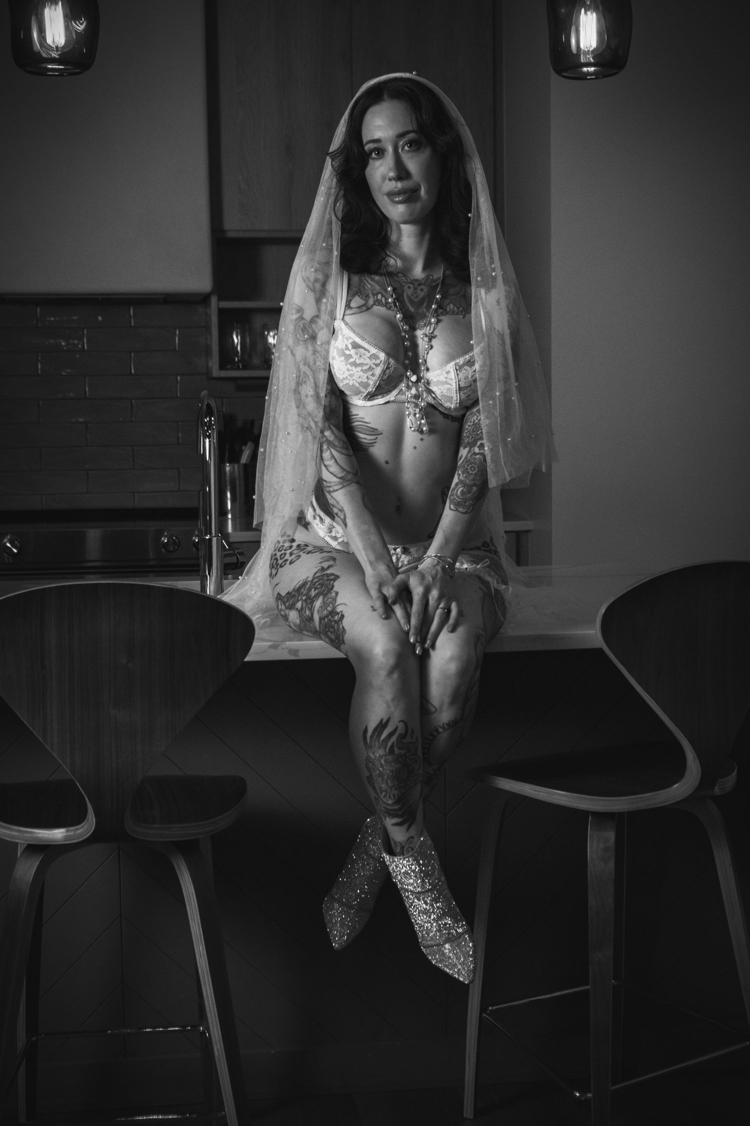 Monochrome bridal boudoir portrait on bar stool featuring delicate veil and lace details.