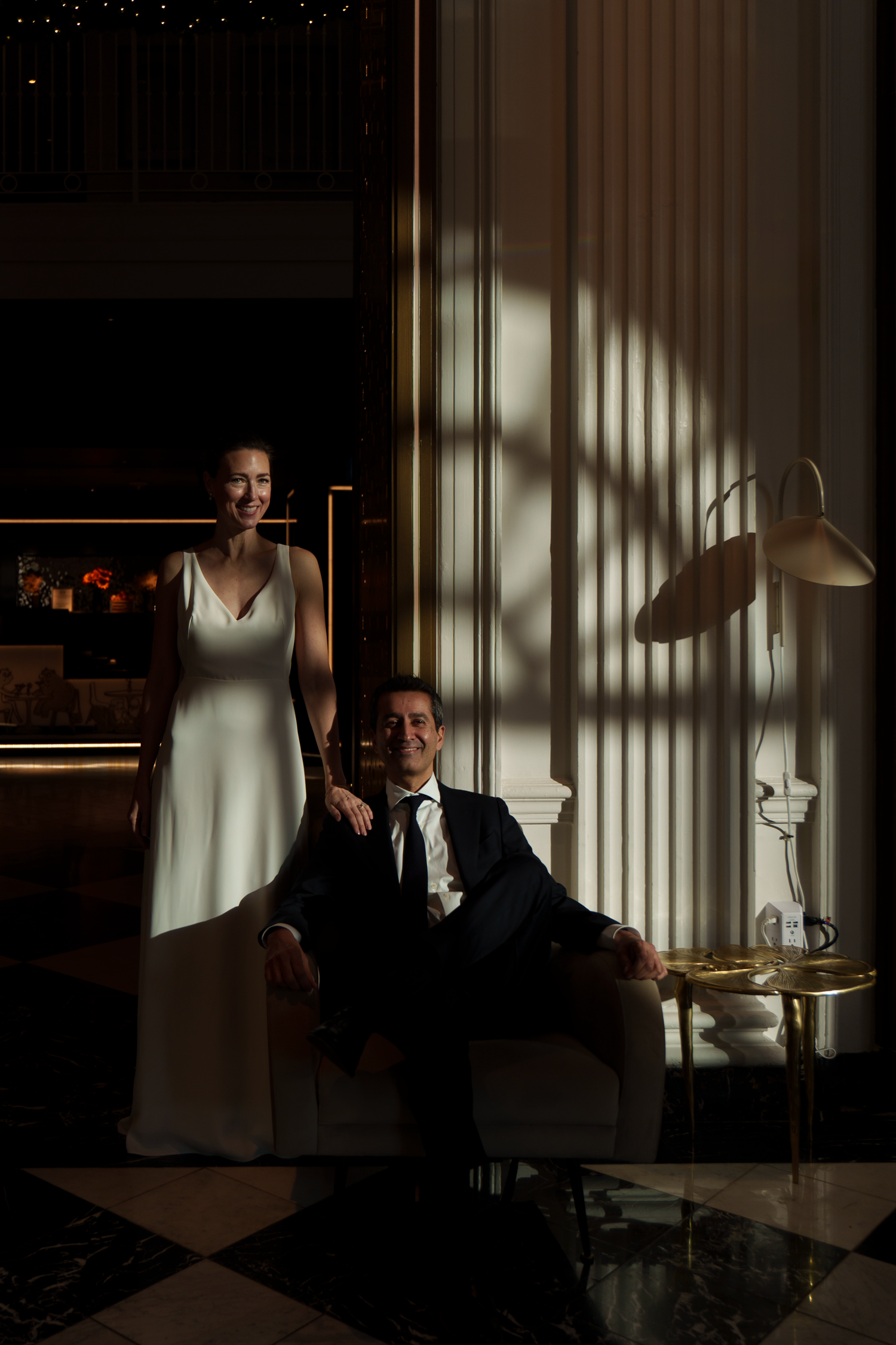 Moody portrait of a couple in wedding attire posed in dramatic lighting with striped window shadows.
