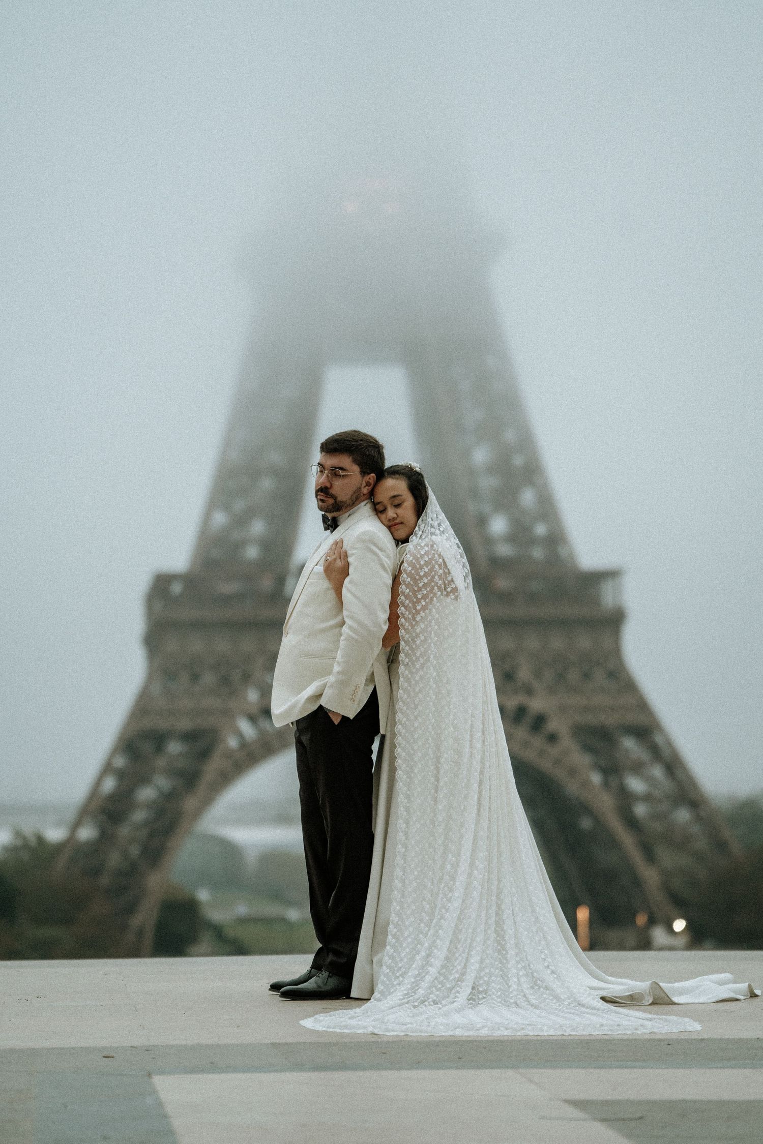 A romantic wedding photo session at the foggy Eiffel Tower with a couple in white dress and black suit.