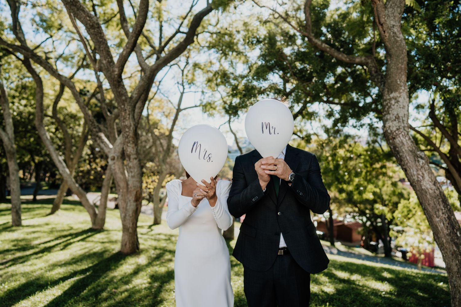 A couple in wedding attire shares a tender moment under sunlit trees during an outdoor ceremony.
