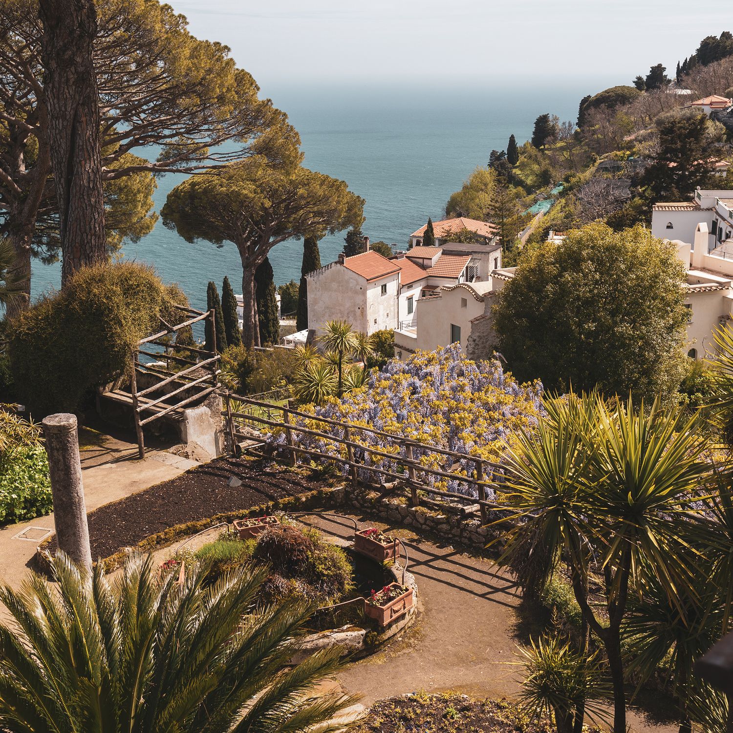 Scenic Mediterranean coastal villa with stone steps and palm trees overlooking the turquoise sea in Ravello, Italy.