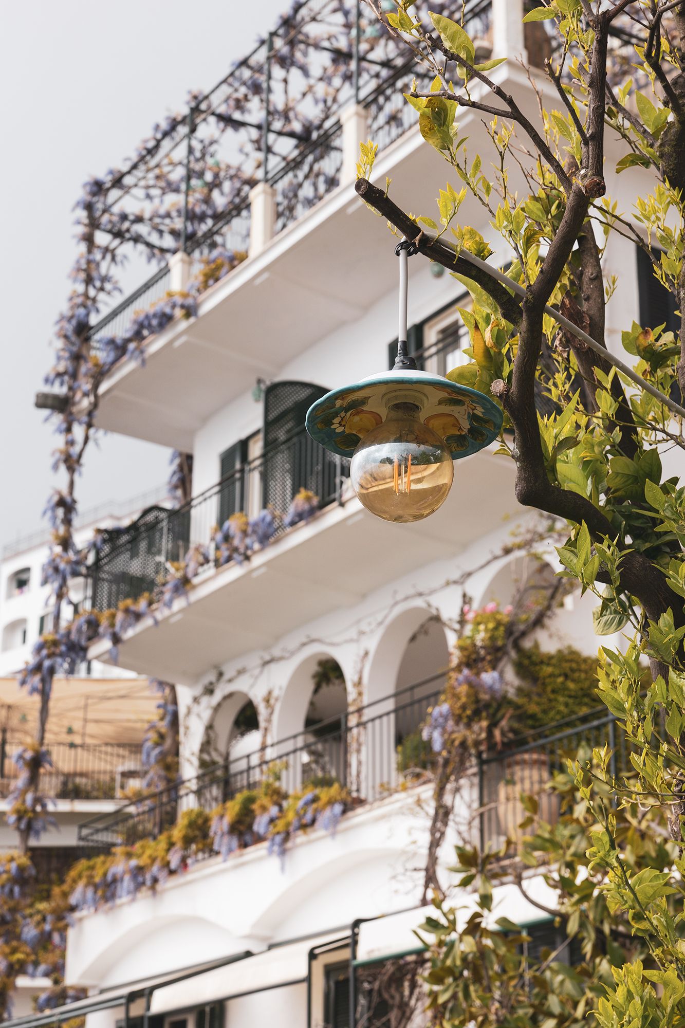 Vintage light bulb decorating an elegant Mediterranean balcony with arched architecture and climbing vines in sunlight.