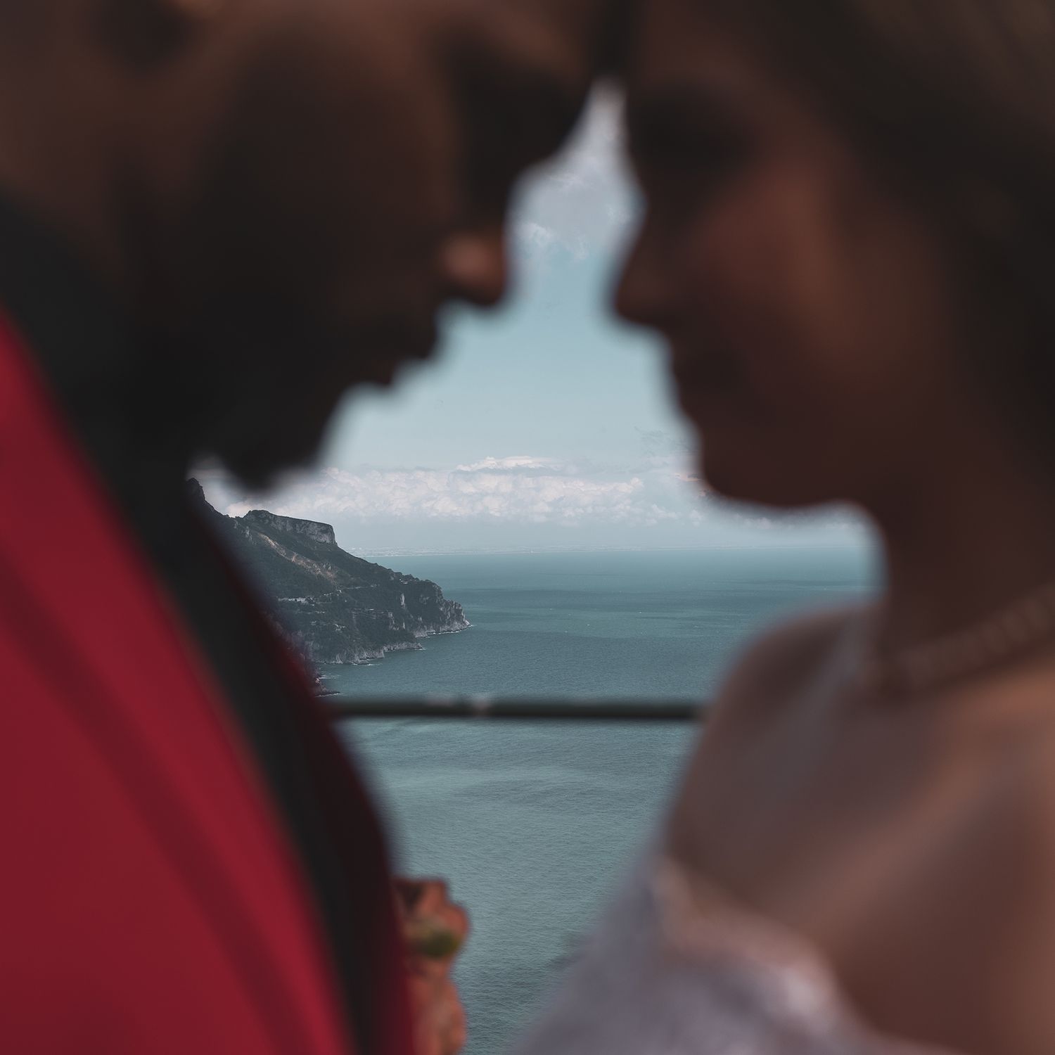 Silhouetted couple in intimate moment against scenic coastal cliff backdrop with misty blue ocean view.