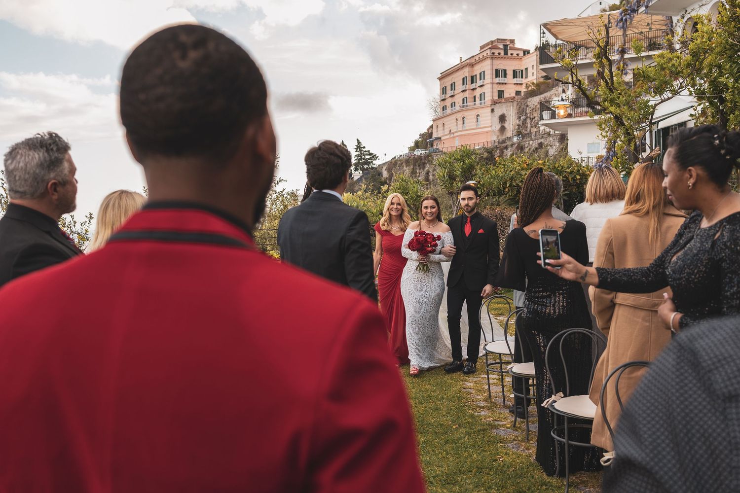 Outdoor wedding ceremony with guests watching bride and groom under cloudy sky.