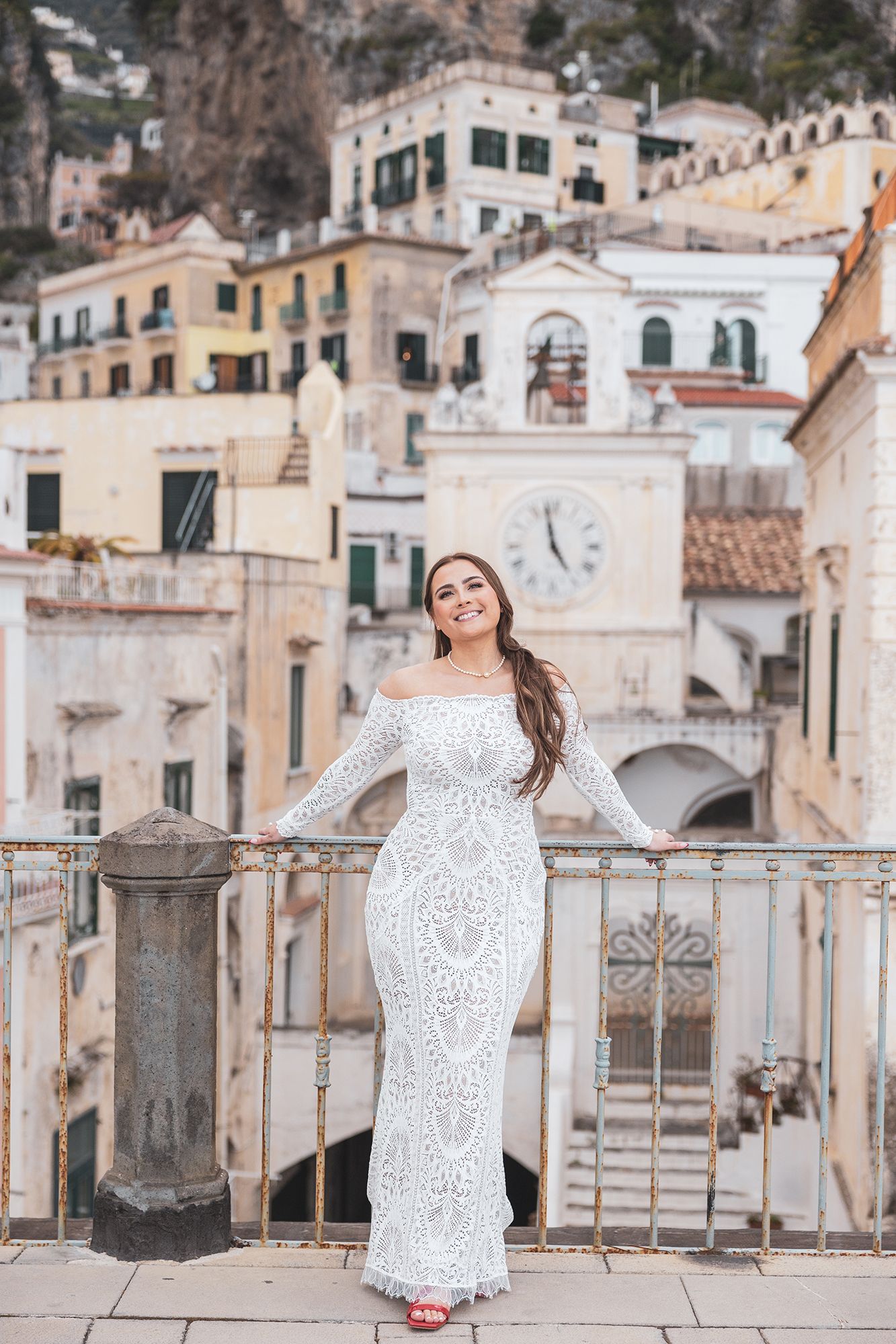 White lace dress photographed against the scenic backdrop of cliffside buildings in Positano, Italy's Amalfi Coast.