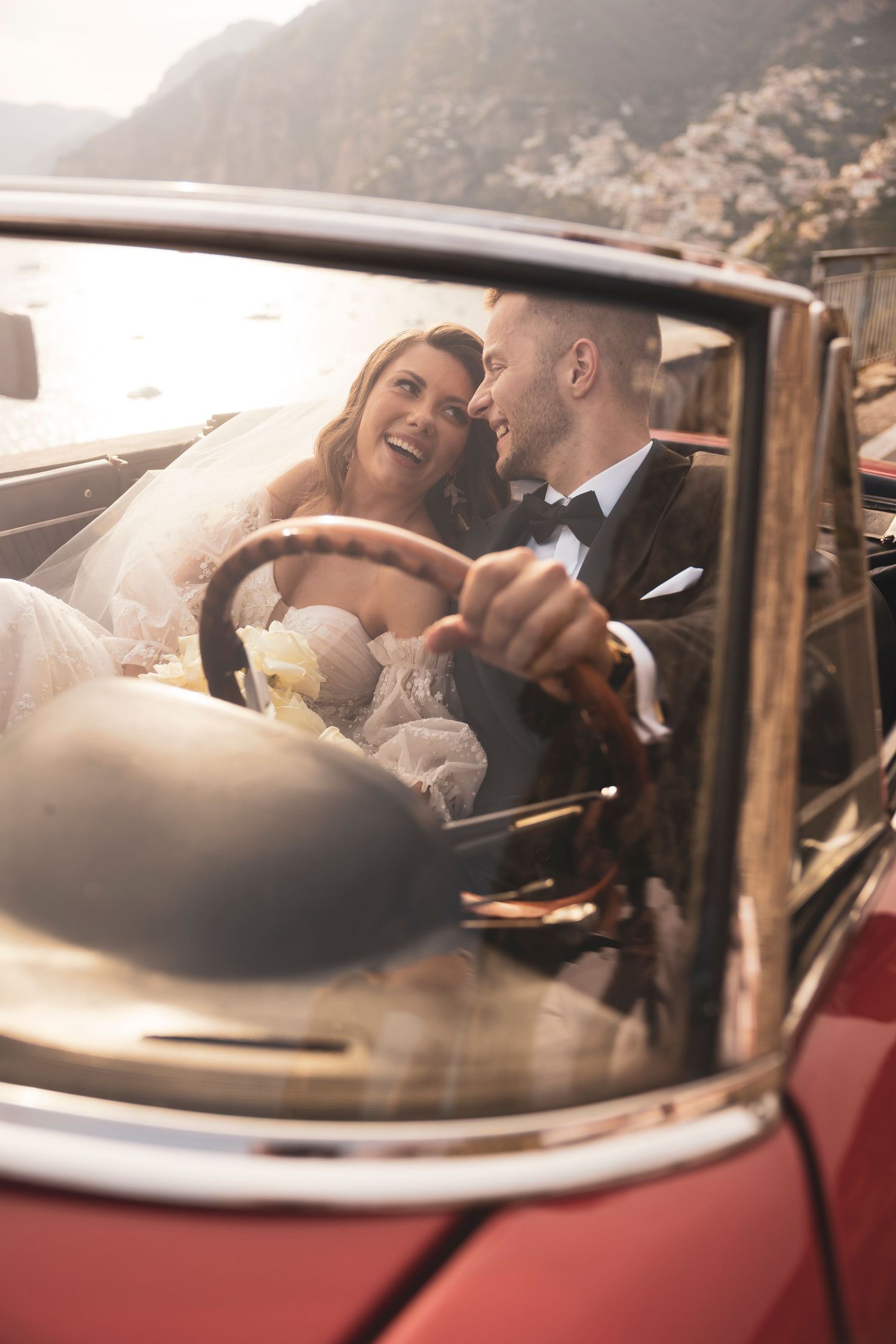 Newlywed couple sharing a joyful moment together in vintage red convertible car on their wedding day.