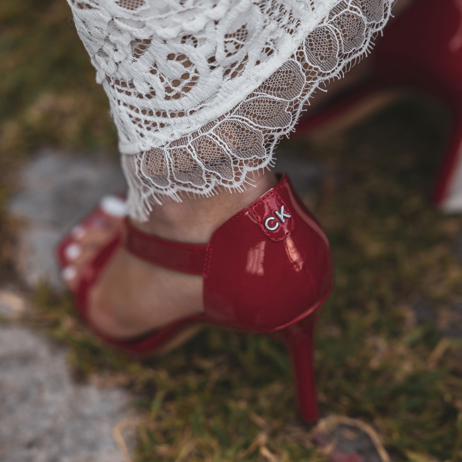 A delicate white lace dress paired with elegant red stiletto heels on grass, showcasing romantic bridal fashion details.