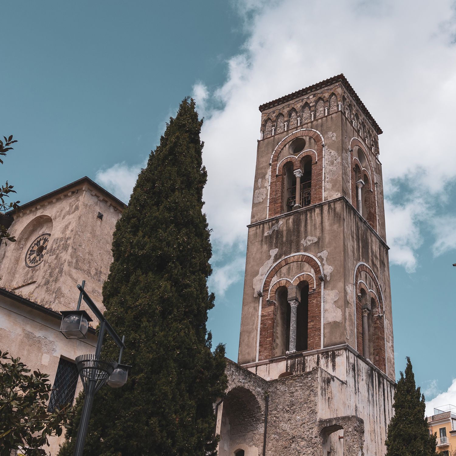 Medieval bell tower and cypress tree against blue sky at Ravello Cathedral on Amalfi Coast, Italy.