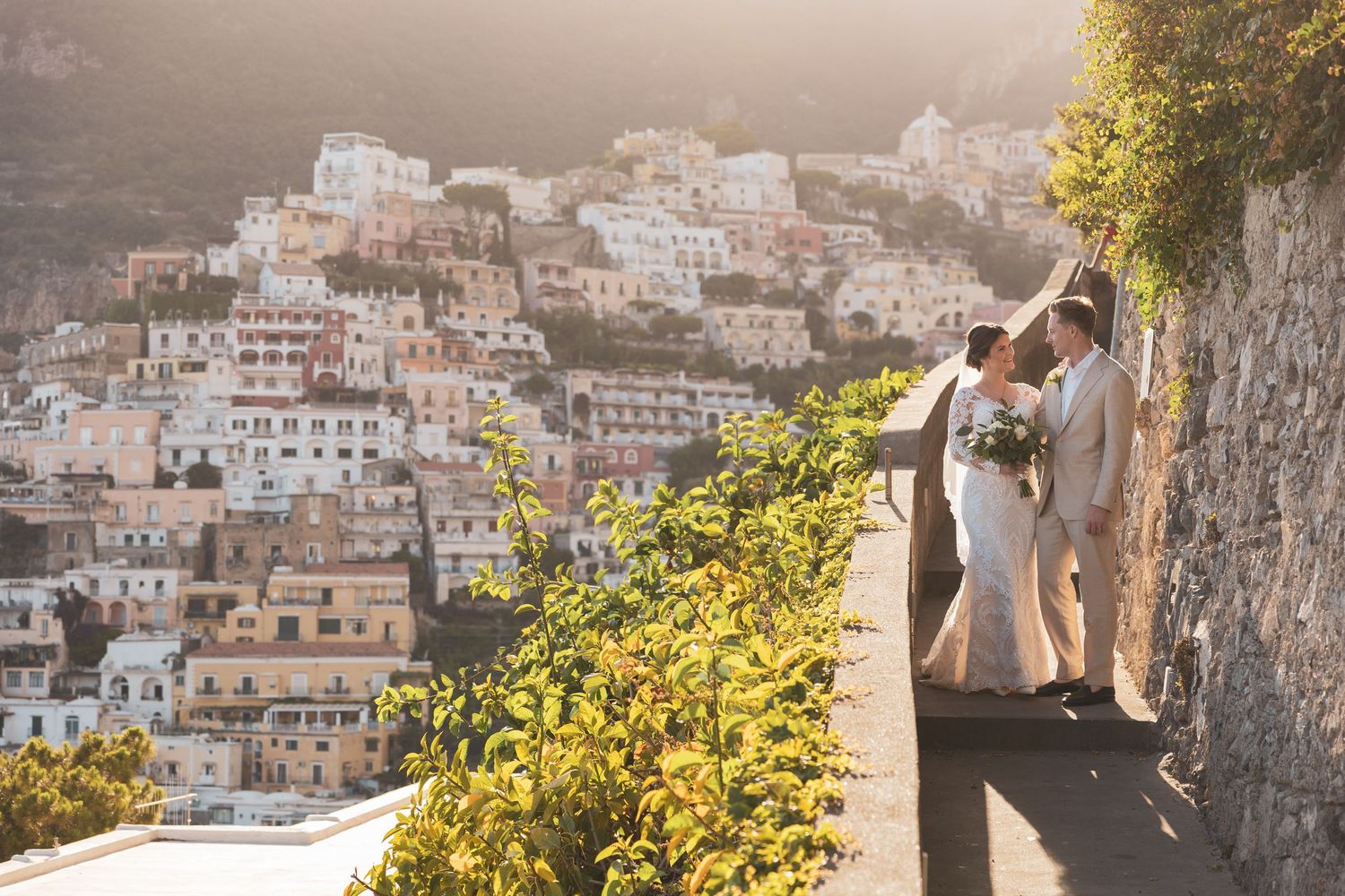 A scenic view of the Amalfi Coast hillside with white buildings cascading down the mountainside at sunset.